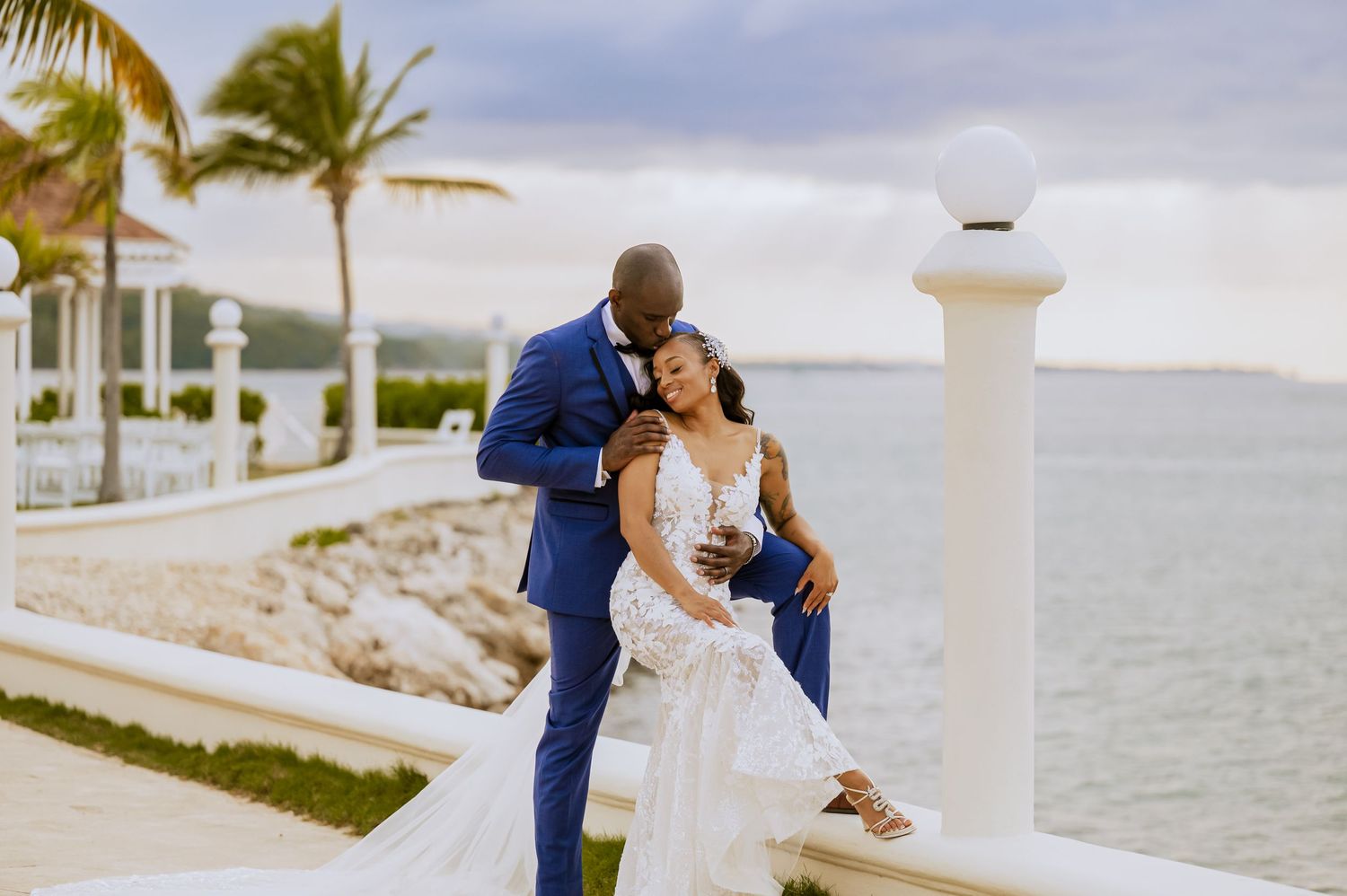 A romantic seaside wedding photoshoot with palm trees and white railings along the waterfront.