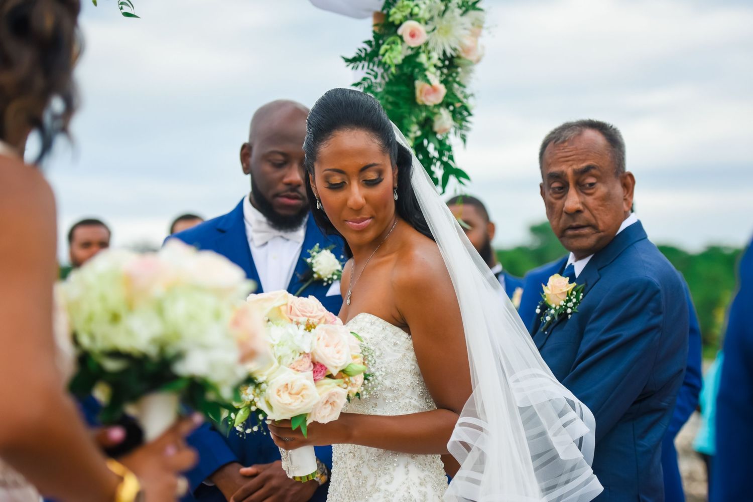 Intimate wedding ceremony moment under floral arch with white and peach blooms.
