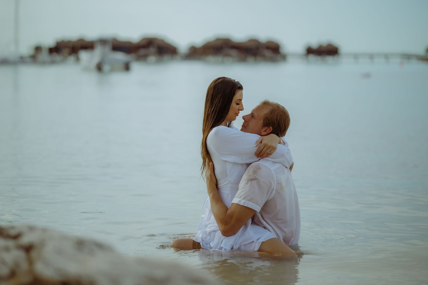 A couple embraces in shallow ocean waters during a romantic beach photoshoot.