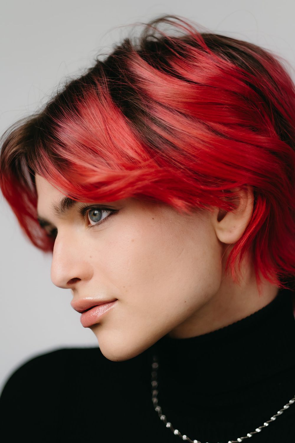 A striking profile view of vibrant red and black layered hair styled in an edgy cut against a light gray background.
