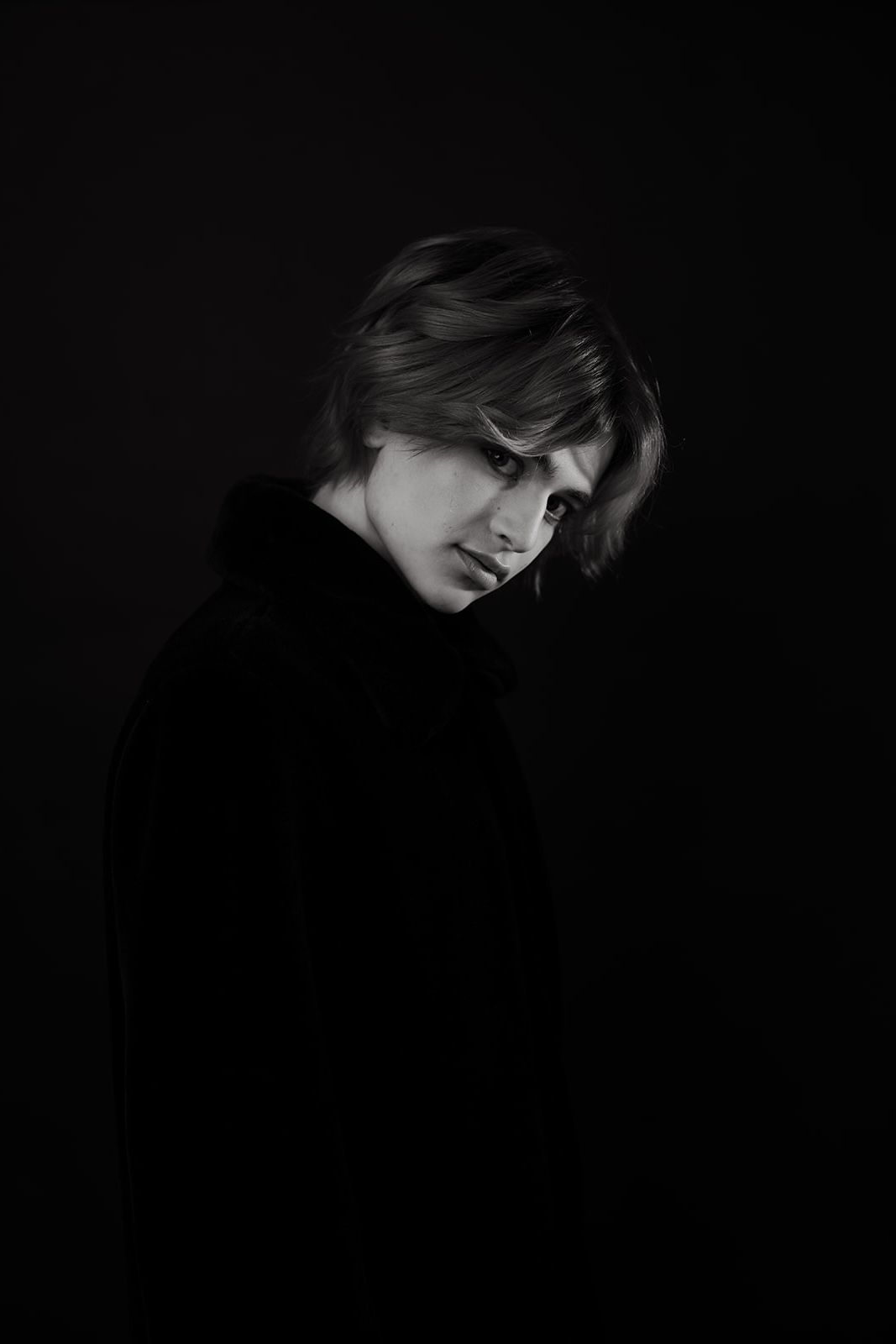 Dramatic black and white portrait showing dark silhouette with hair falling across face against shadowy background.