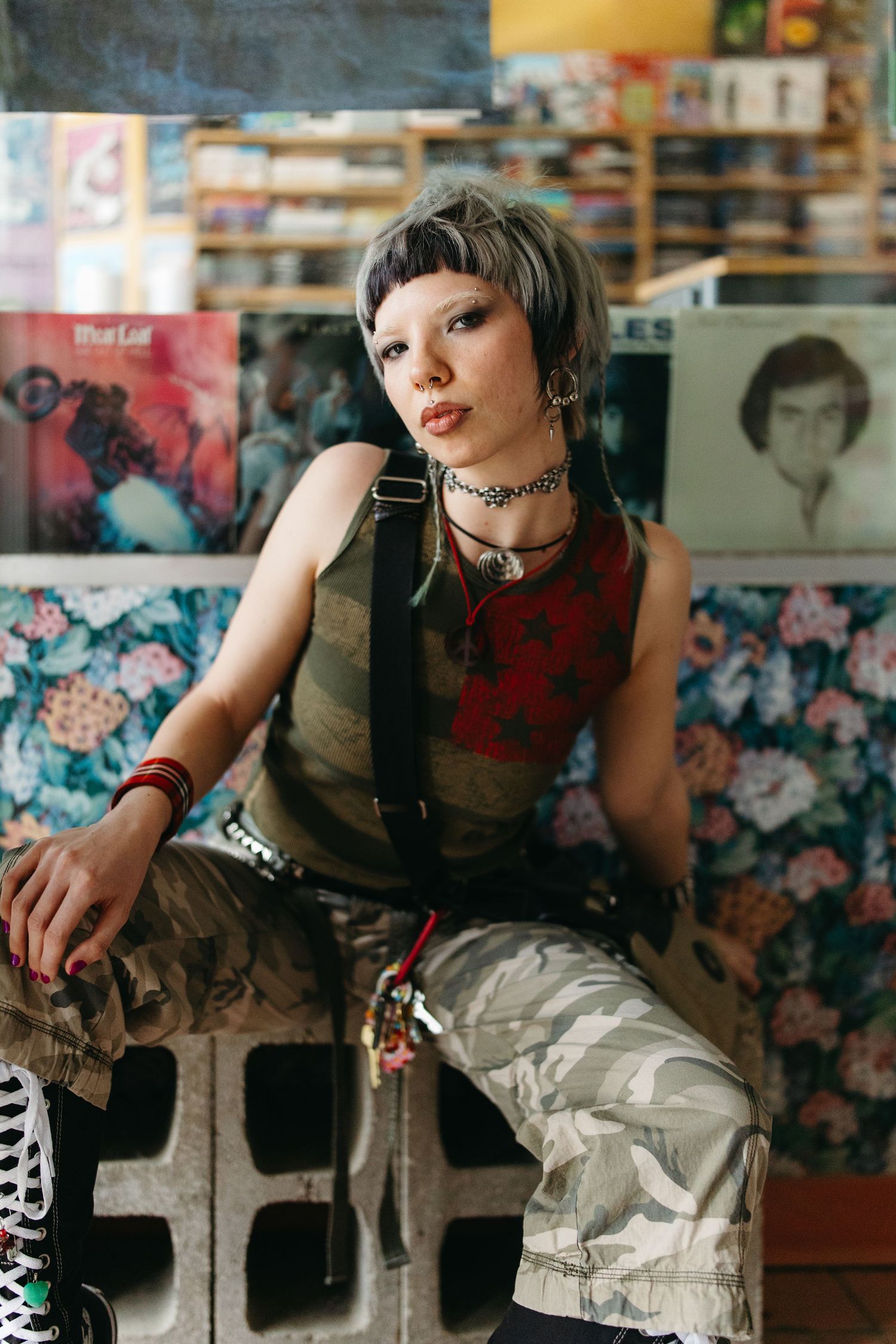 Alternative fashion portrait in casual setting with cargo pants and punk rock aesthetic against floral wallpaper.