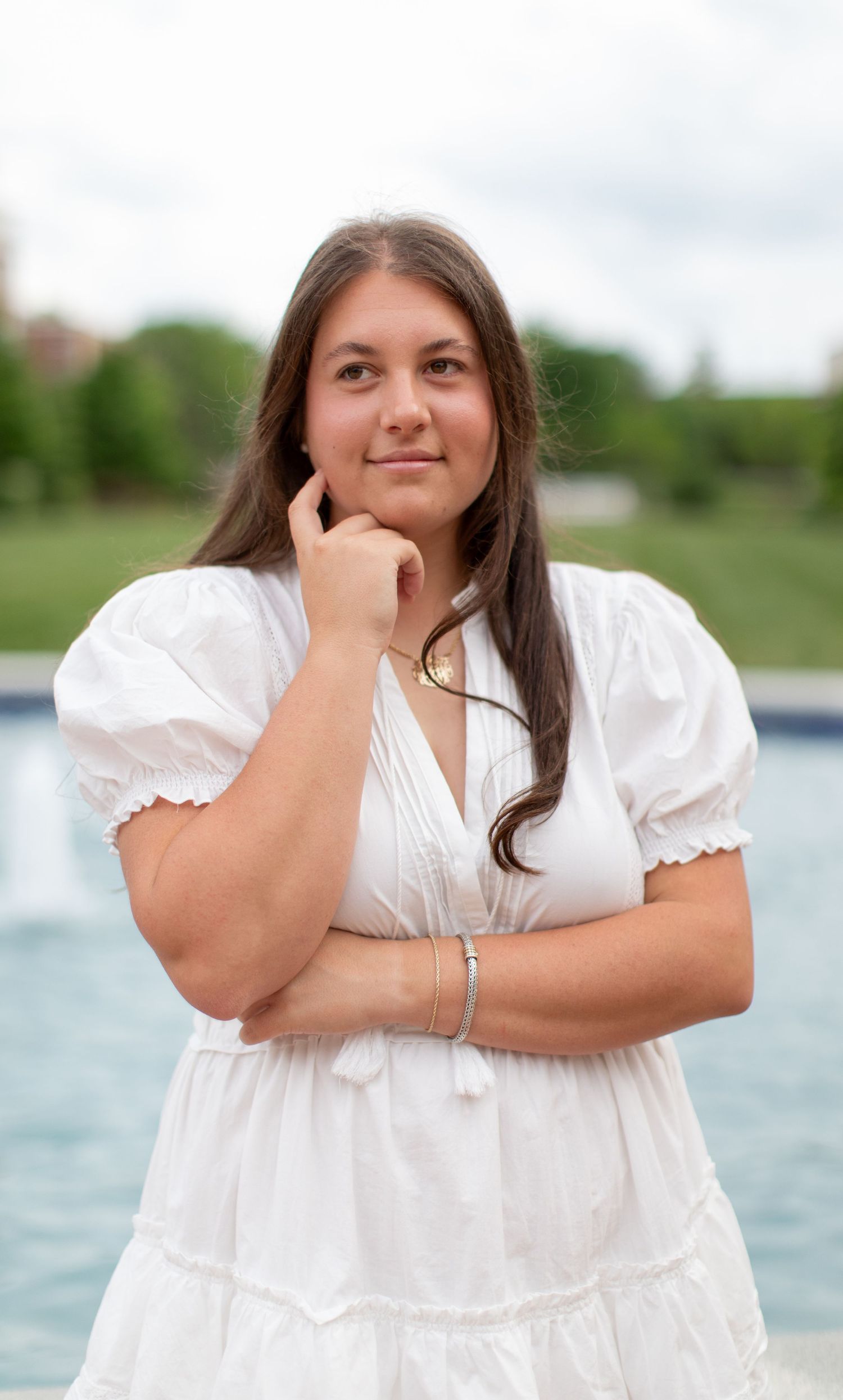 Senior portraits taken by a lake featuring a white summer dress and natural poses.