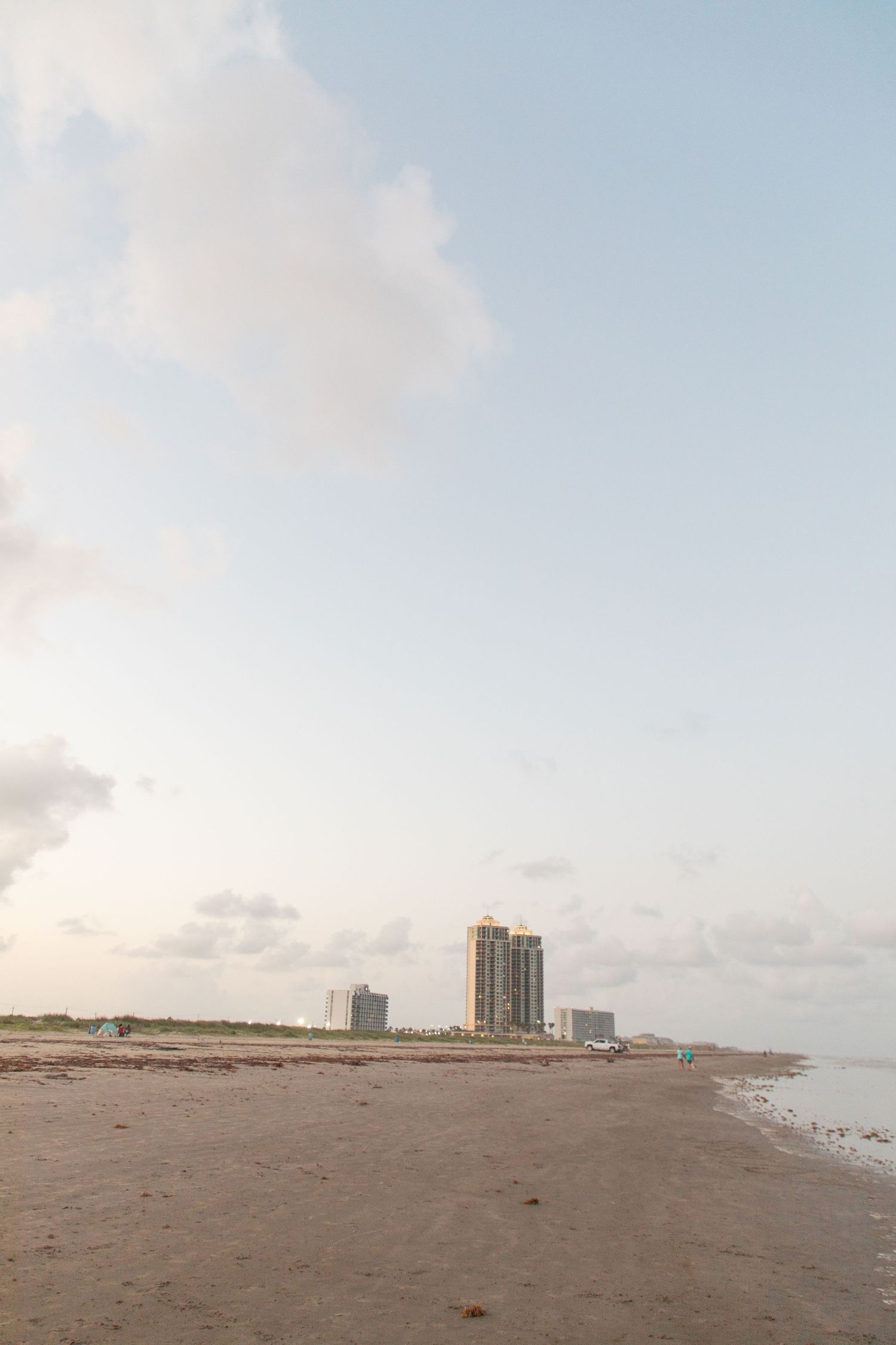 Empty beach landscape with distant high-rise buildings under blue sky.