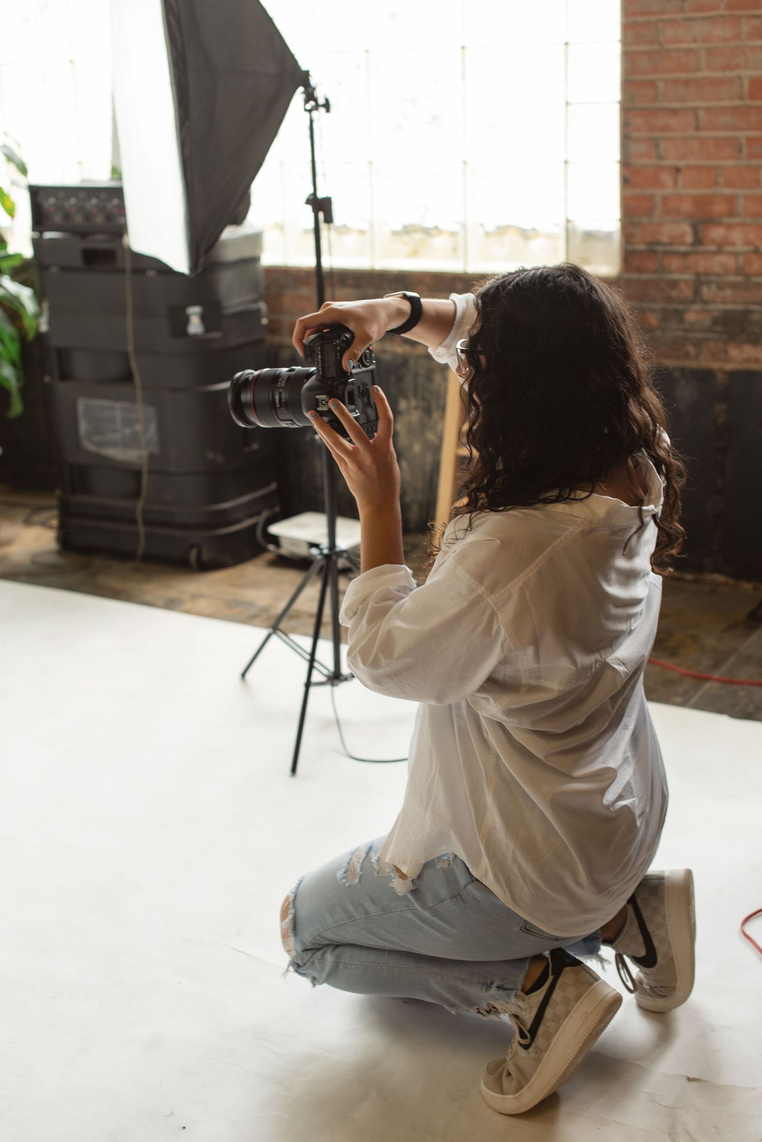 Photographer in casual attire taking pictures while kneeling on studio floor.