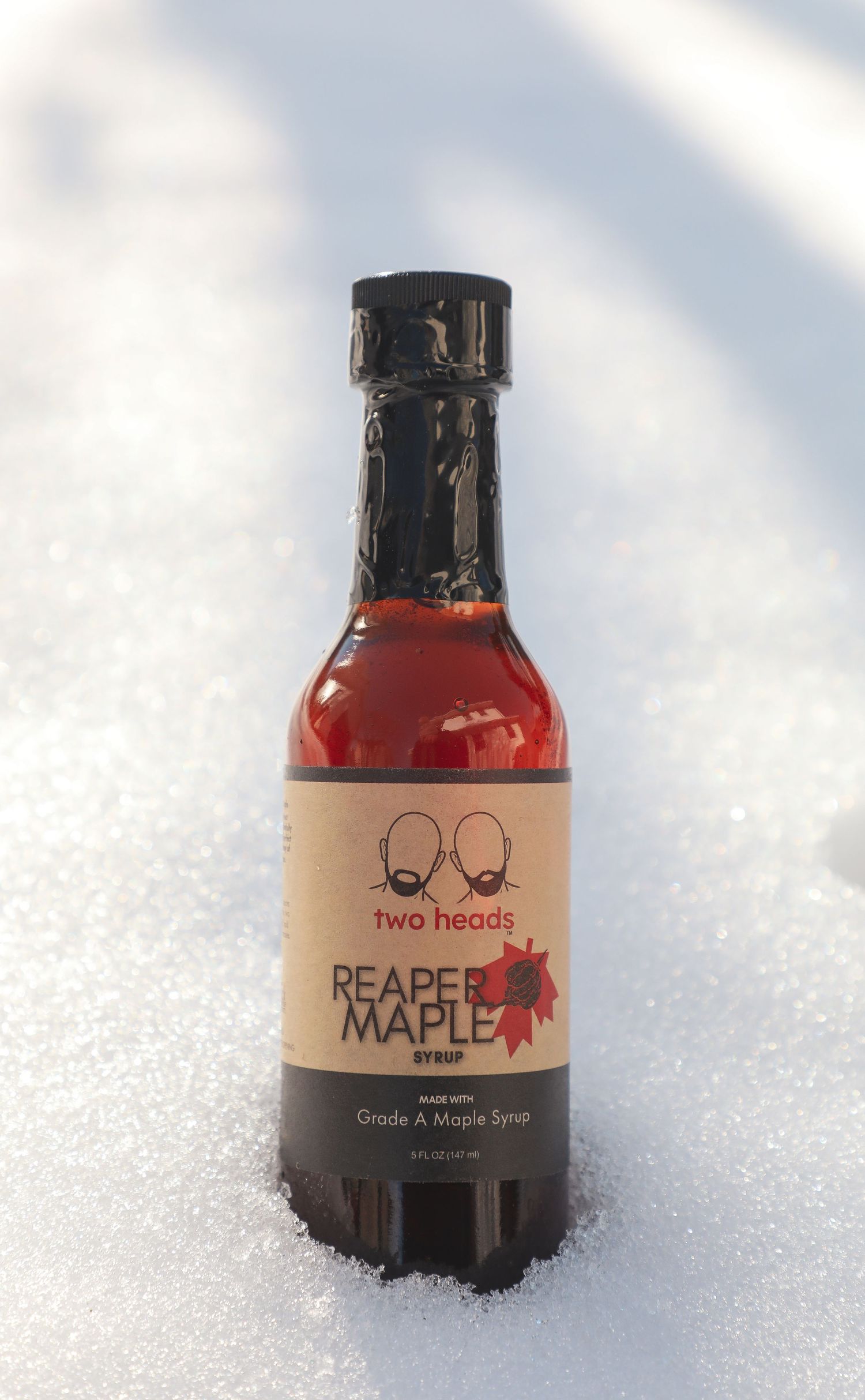 Three bottles of Two Heads maple syrup products arranged in snow with winter lighting.