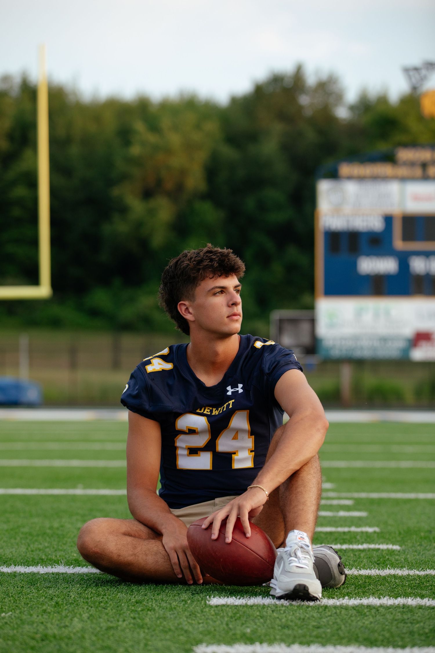 High school football player posing for portraits on field in navy uniform.