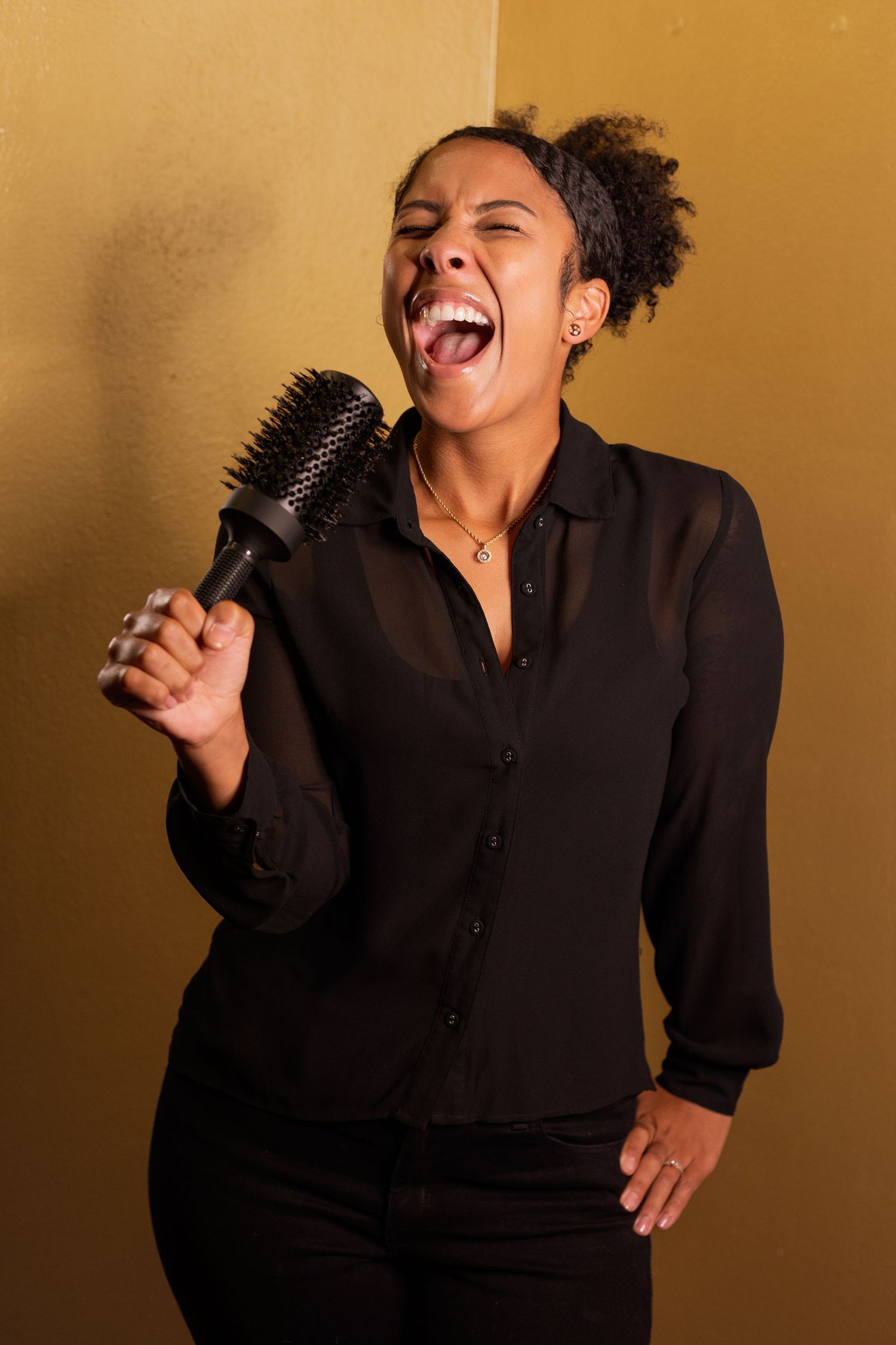 Person in black shirt laughs joyfully during expressive portrait session against warm background.
