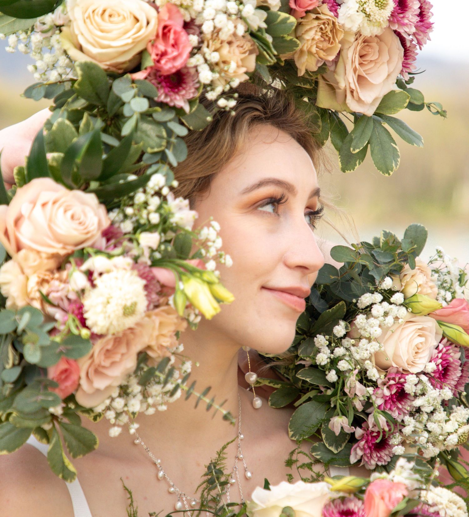Close-up of delicate floral crown with roses, baby's breath and greenery in soft natural lighting.