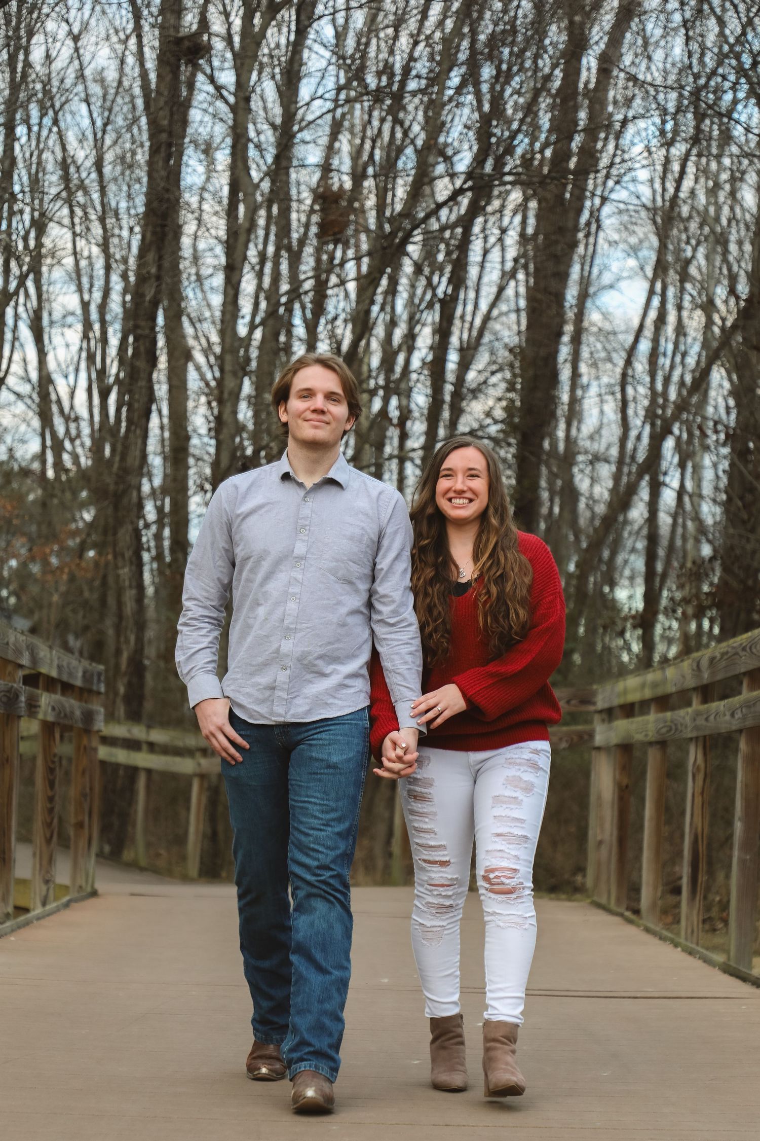 A couple walks together on a wooden boardwalk path through bare winter trees.
