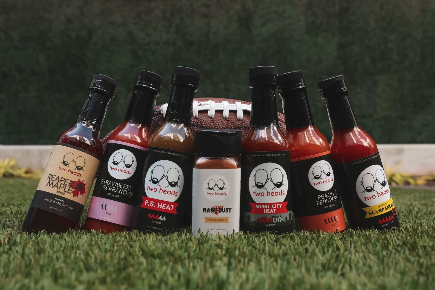 Collection of sauce bottles with cute cartoon face labels lined up on grass.