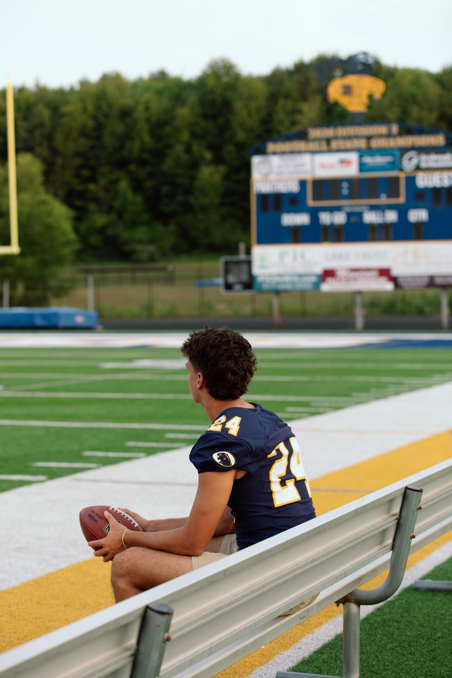 Person sitting alone on bleachers at a football field with scoreboard in background.