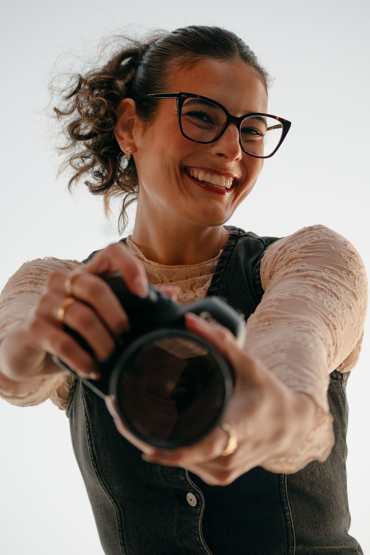 Photographer in glasses and vintage dress takes selfies while holding professional camera.