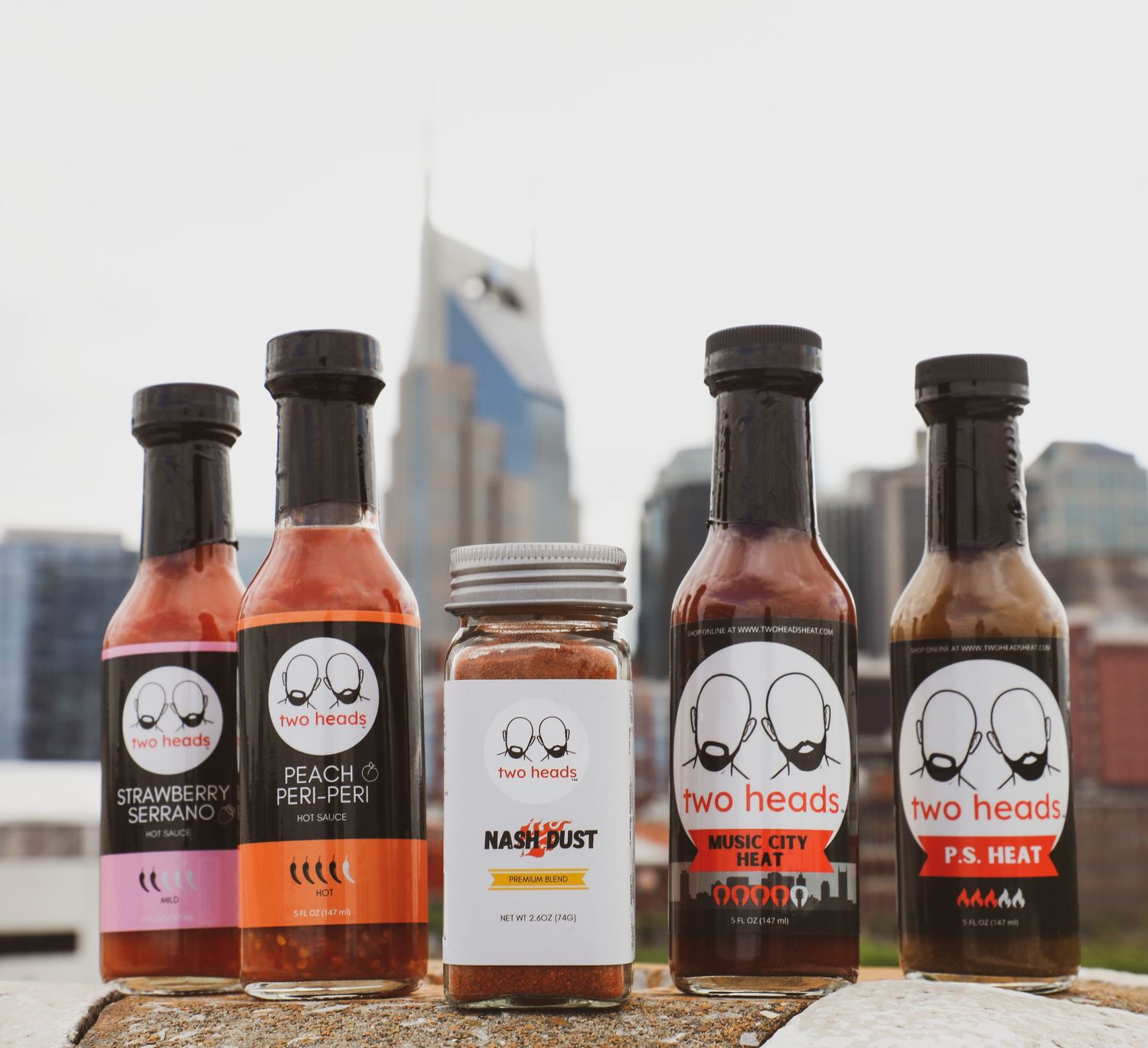 Row of artisanal hot sauce bottles with minimalist black and white label designs displayed against a blurred background.