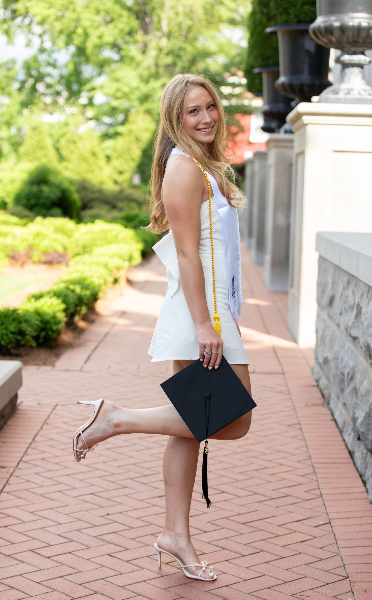 Outdoor graduation photo session showing playful poses on a brick walkway in front of stone columns.