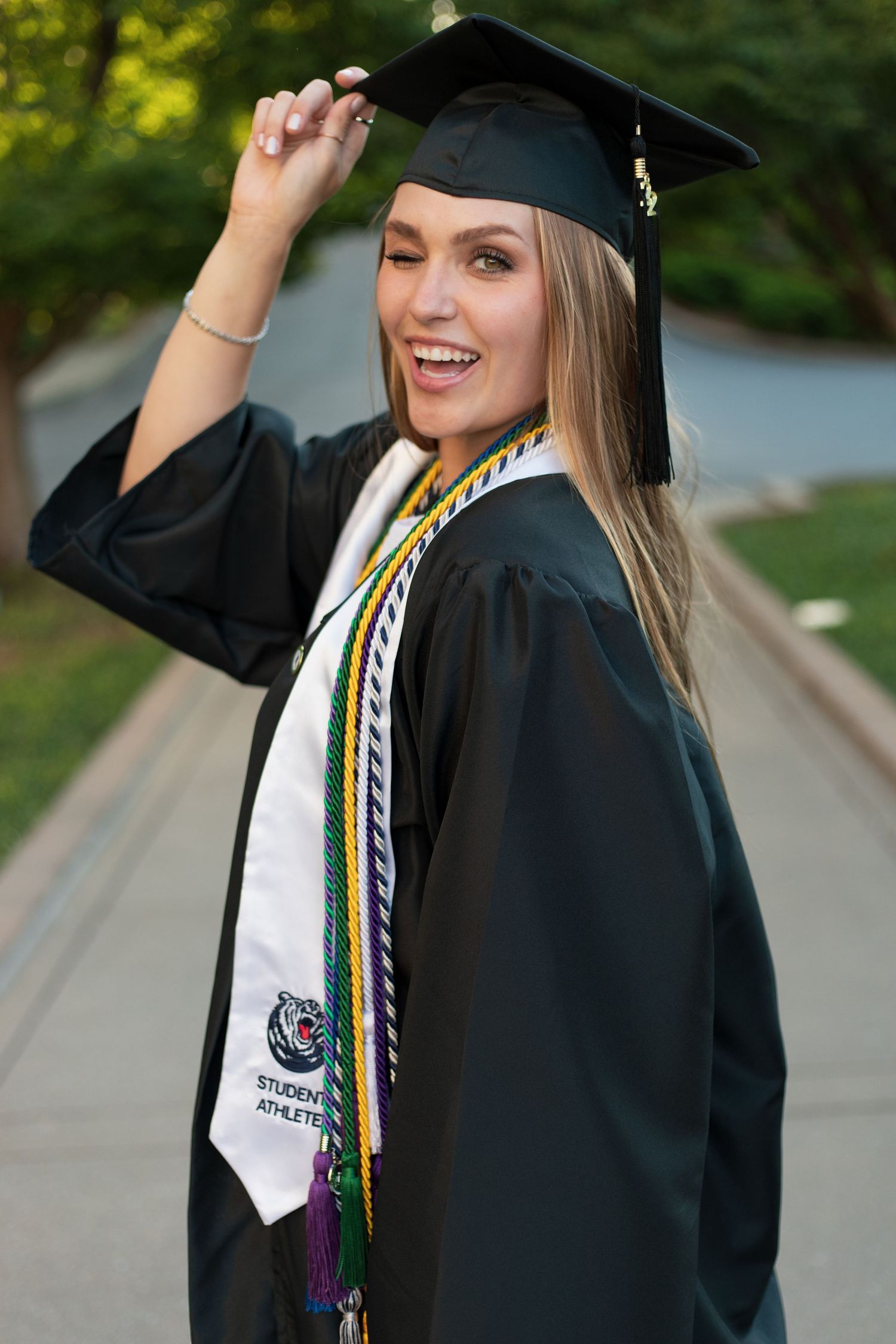 Graduate in black cap and gown with decorative stole posing outdoors.