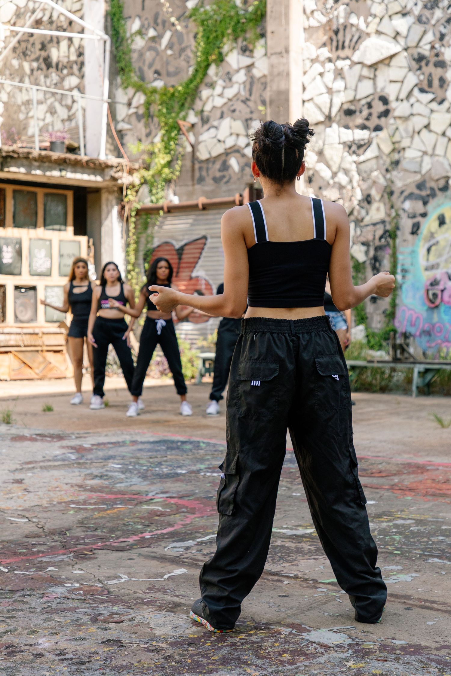 People in black outfits dancing in urban setting with graffiti walls.
