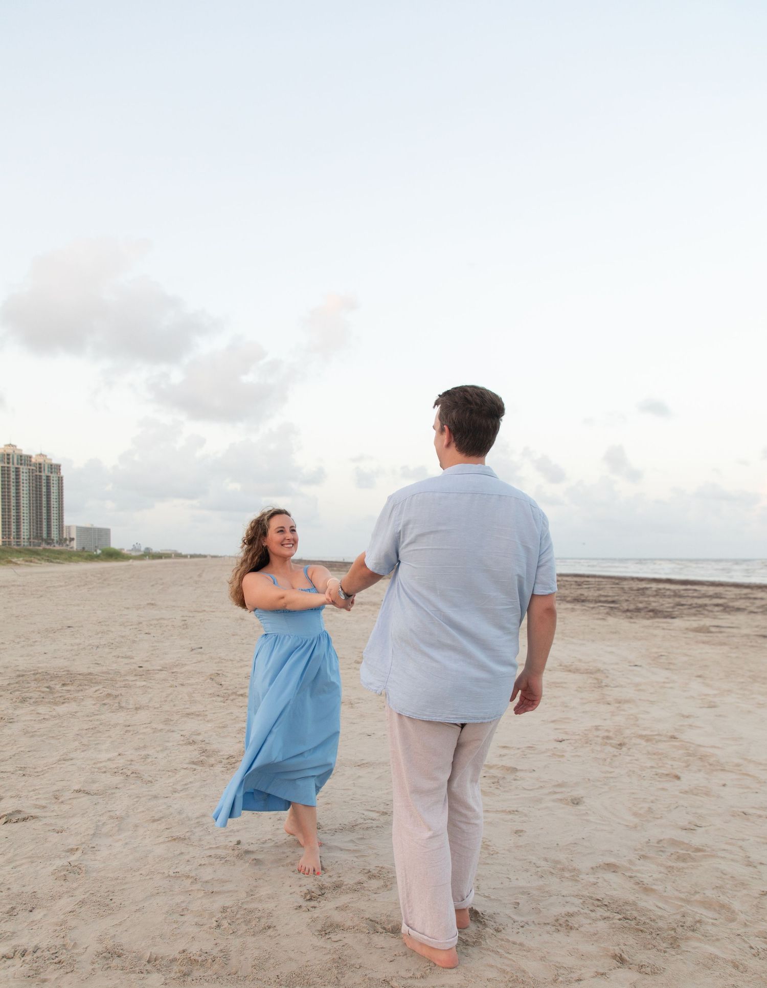 A couple dances playfully together on a sandy beach at sunset.