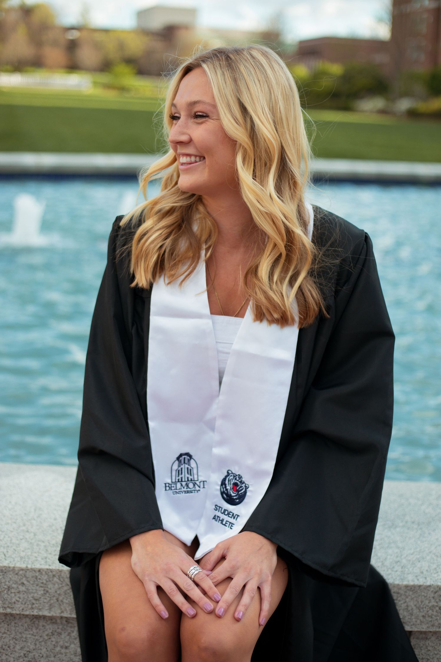 Graduate in black robe poses with diploma by waterfront in series of celebratory shots.