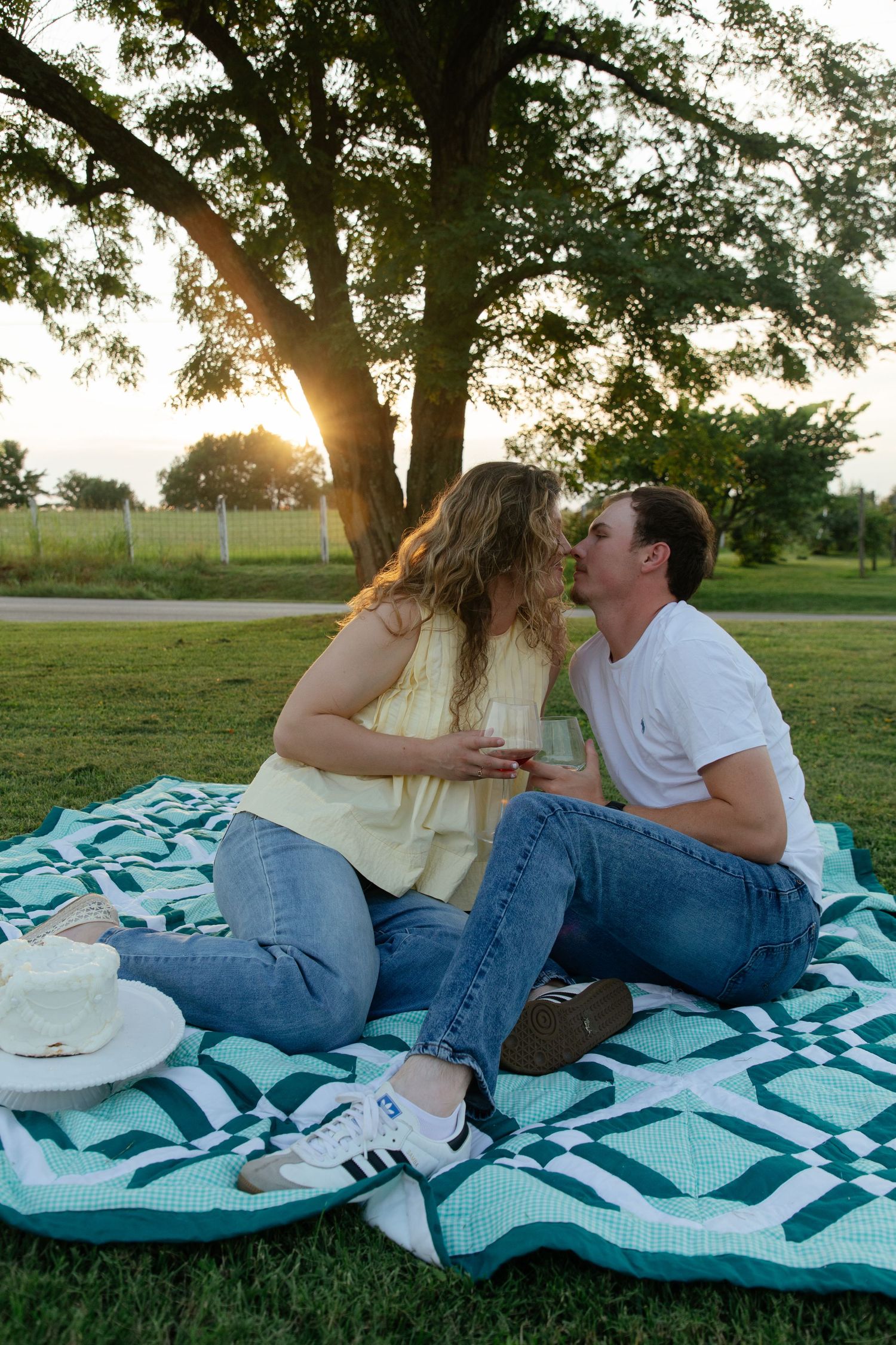 Couple relaxing on blue and white blanket under trees during golden hour sunset.
