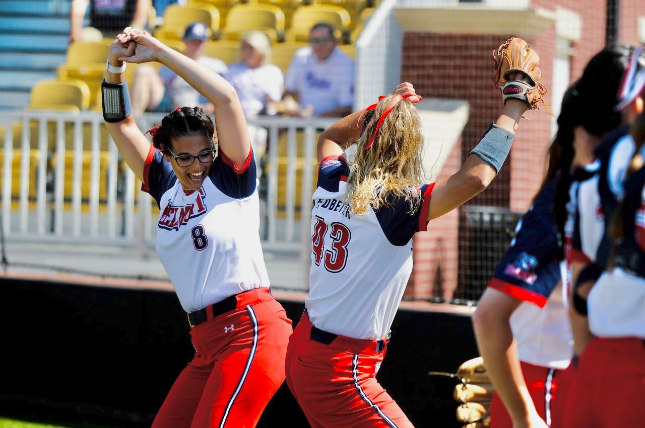 Softball players celebrating and cheering during competitive game on sunny field.