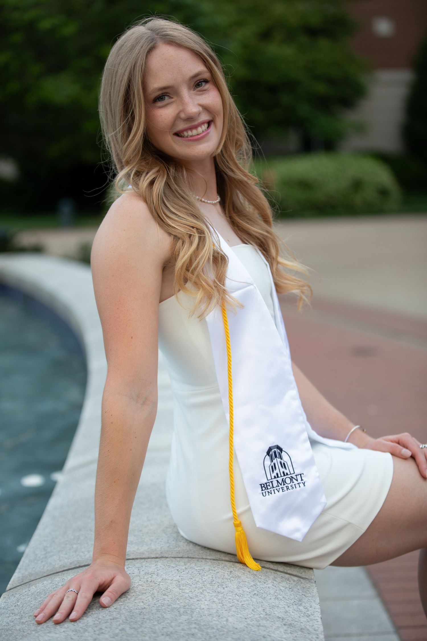 Graduate posing with diploma and yellow tassel against brick walkway background.