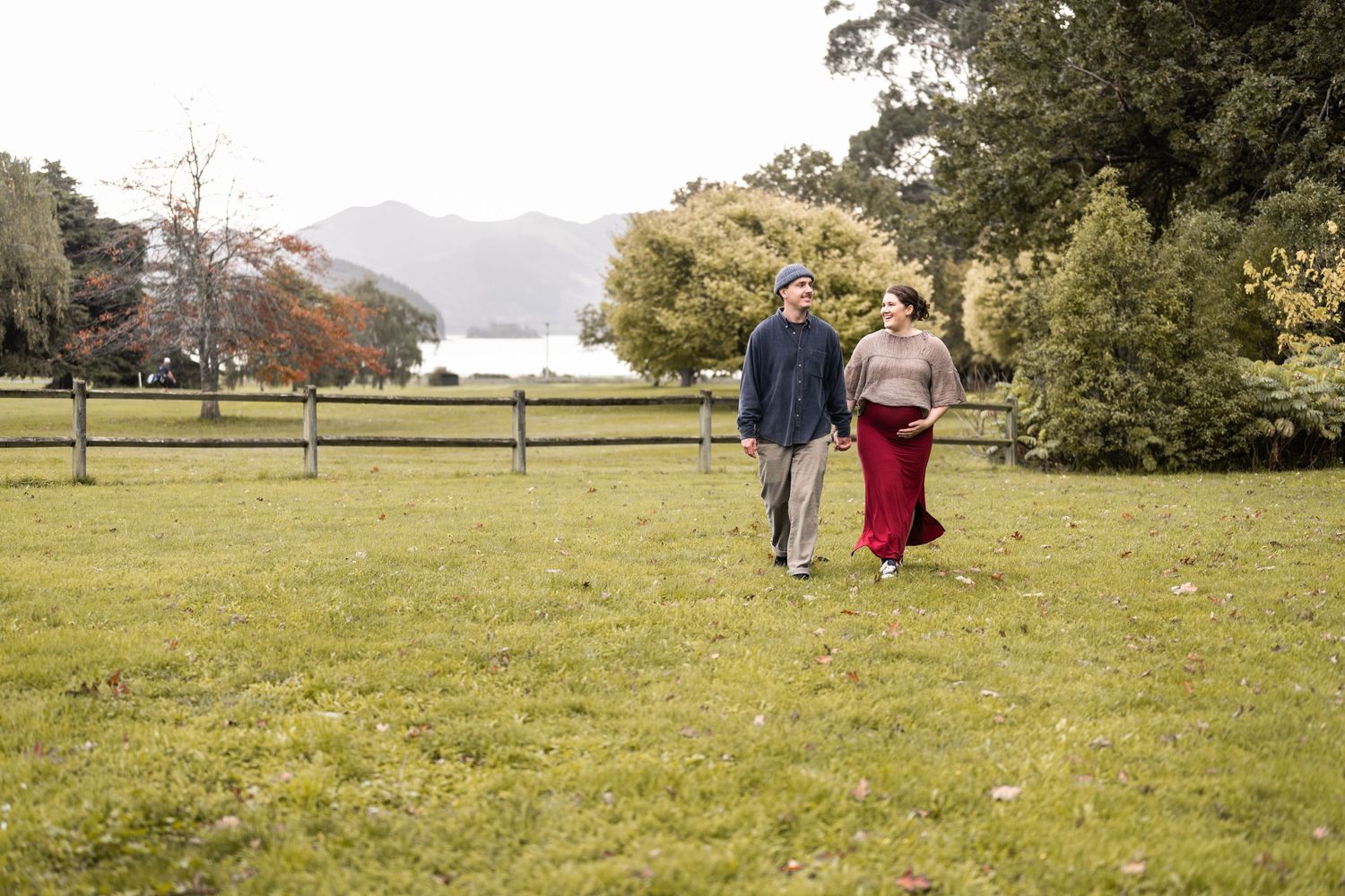 Maternity photography of couple walking in grassy park holding baby bump.