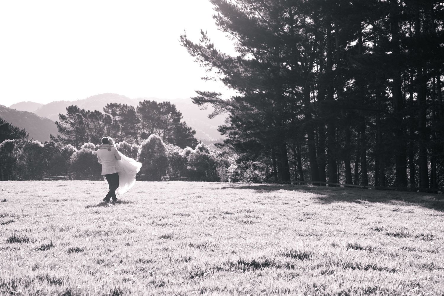 Bride and groom embracing in an open field captured in soft black and white tones.