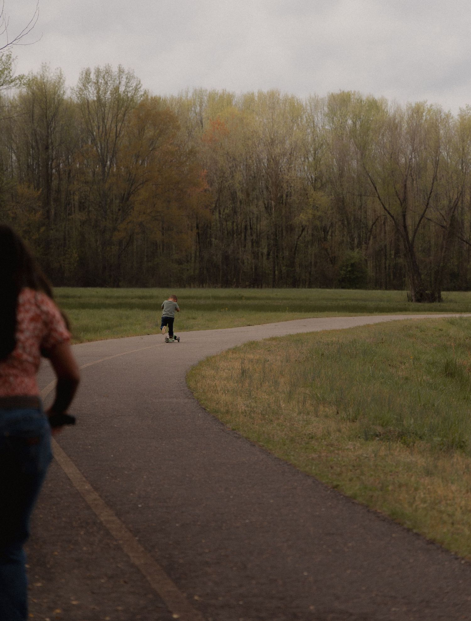 Person skateboarding on a winding path through a green park on cloudy day.