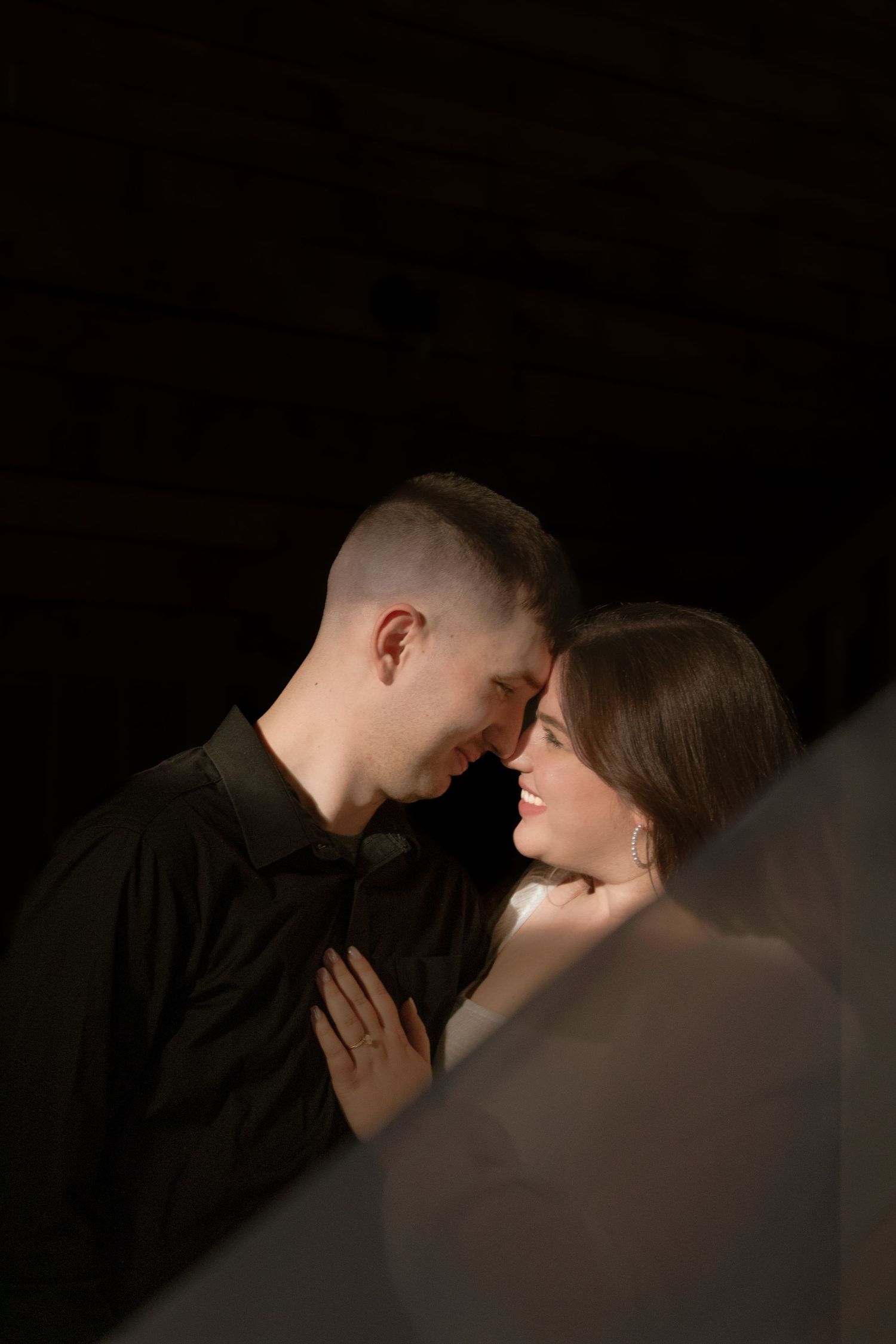 Couple tenderly touching foreheads in a dramatic dark studio portrait.