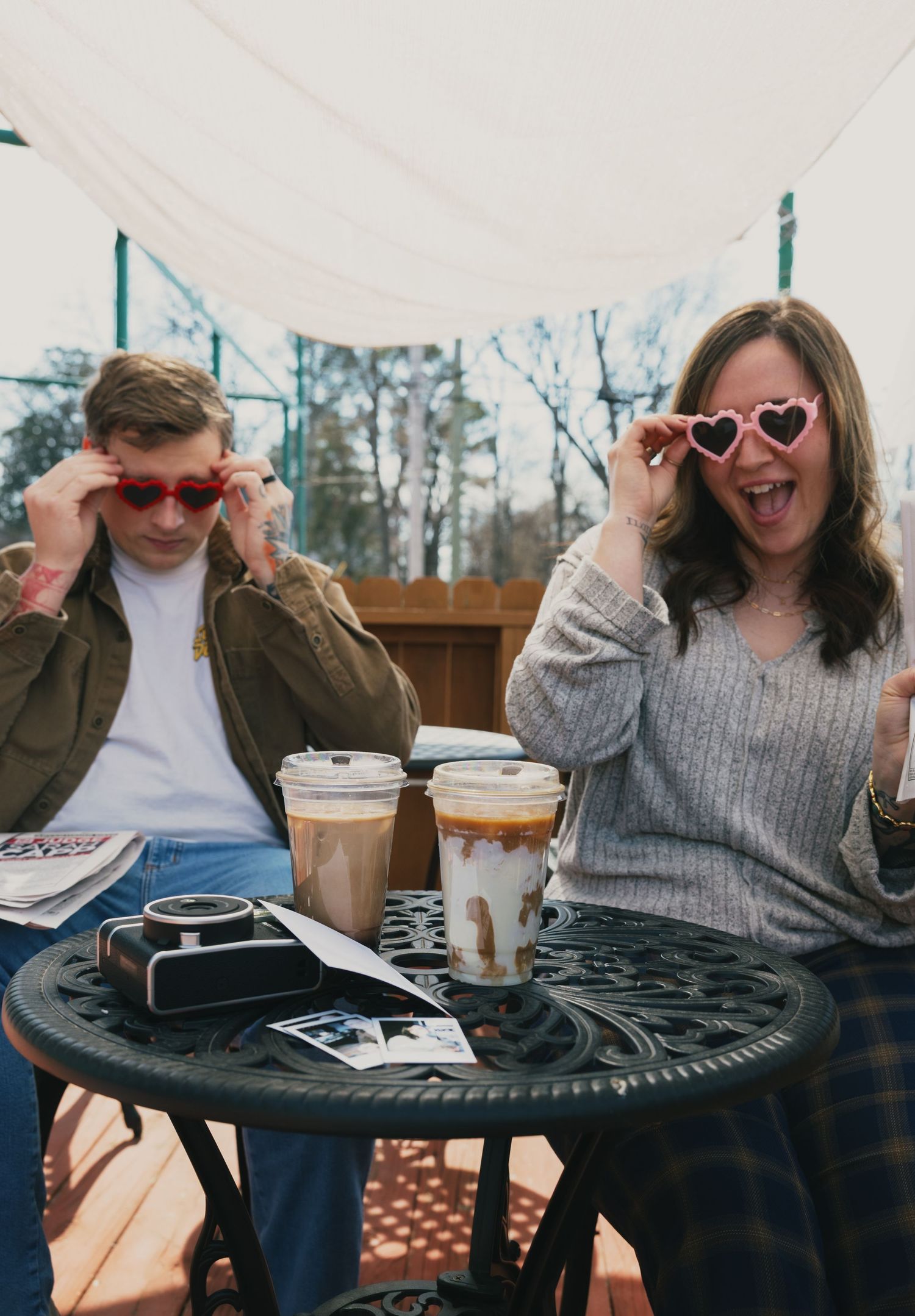 Couple at outdoor cafe table wearing fun heart and red sunglasses with iced coffee drinks.