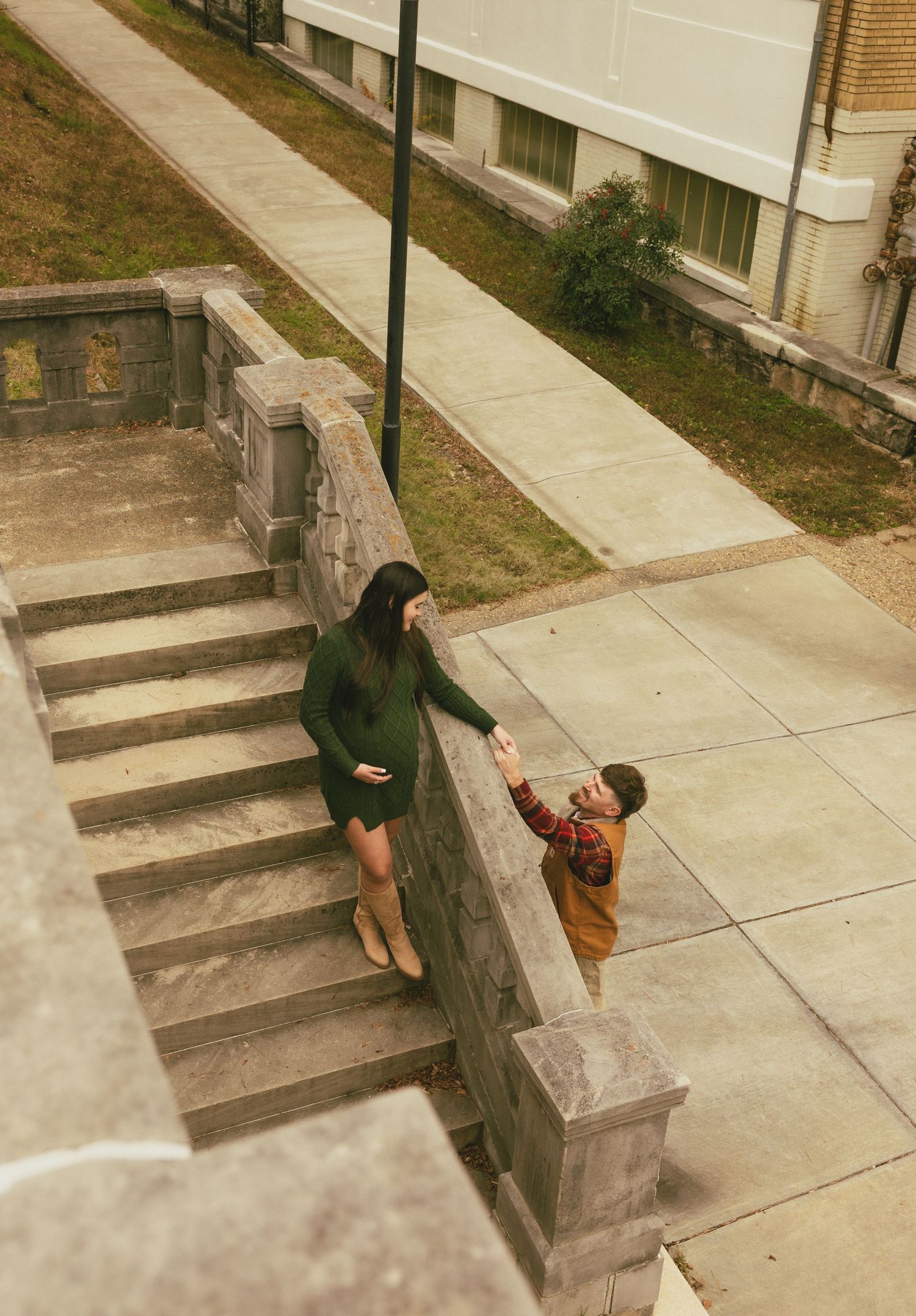 Couple holding hands on stone steps outdoors, woman in green maternity dress.