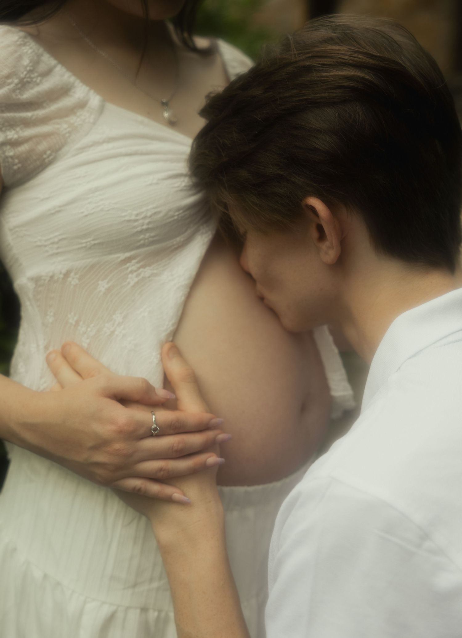 Close-up of a man gently kissing a pregnant woman's belly while holding it with both hands.