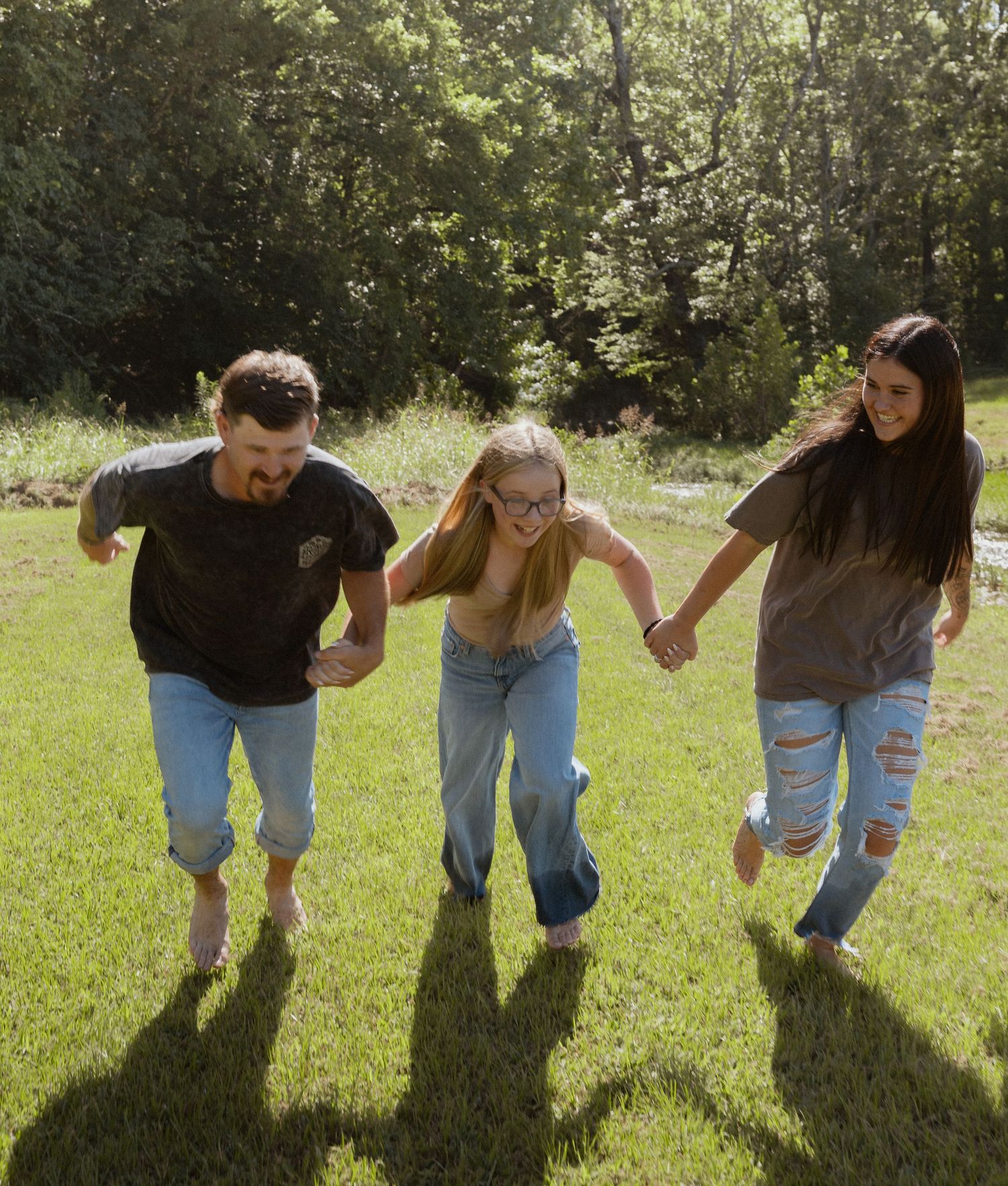 Joyful family of three holding hands and jumping together on a sunny green lawn outdoors.