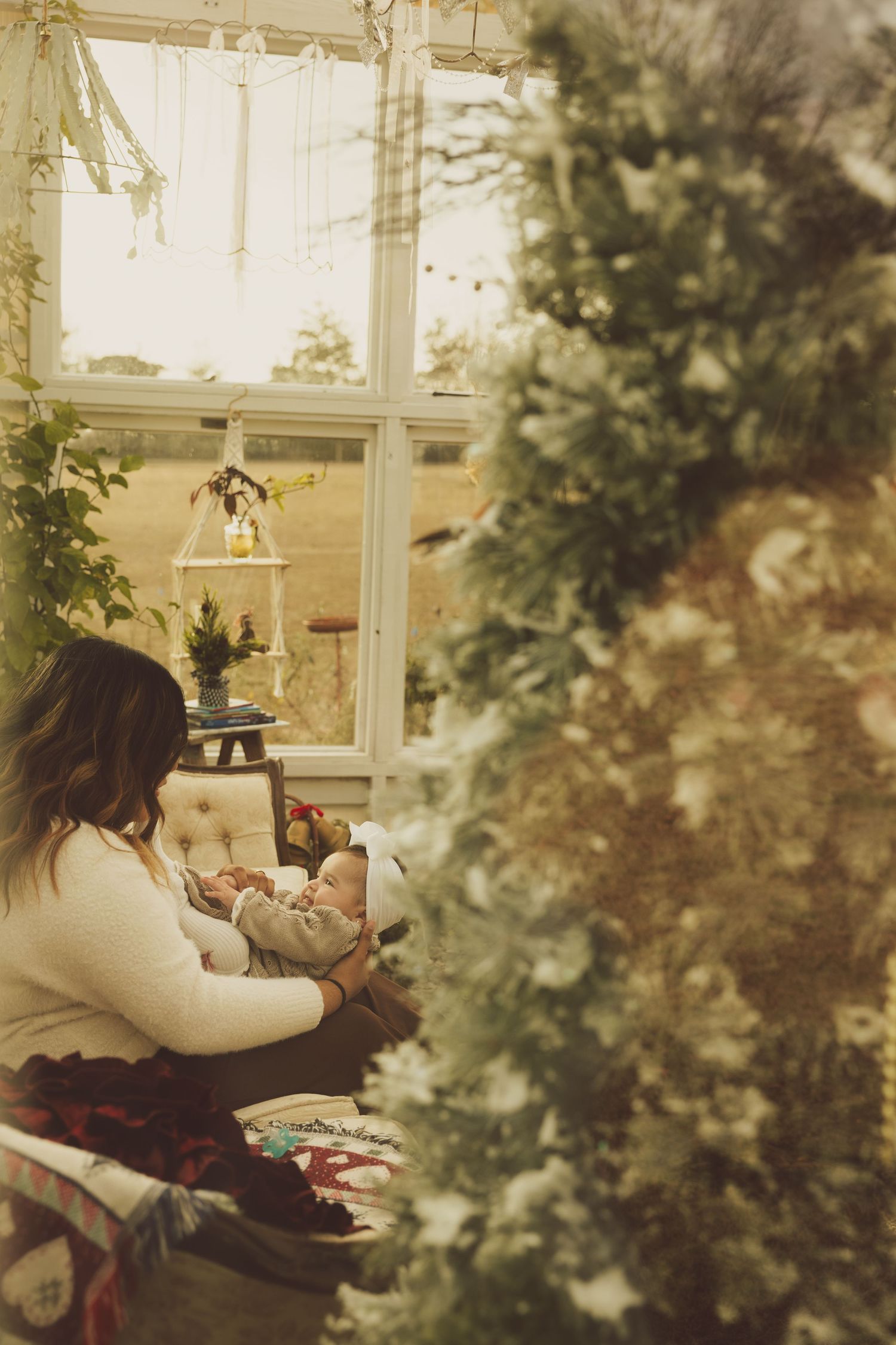 Mother sitting in chair with her newborn baby near large window with warm glowing light.
