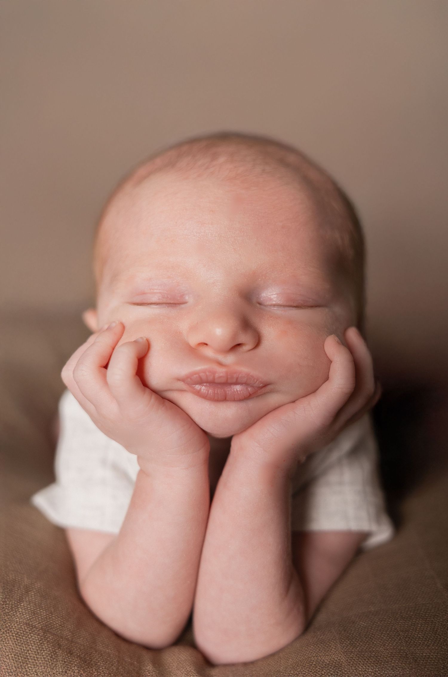Adorable sleeping newborn baby posed with hands under chin in studio portrait.