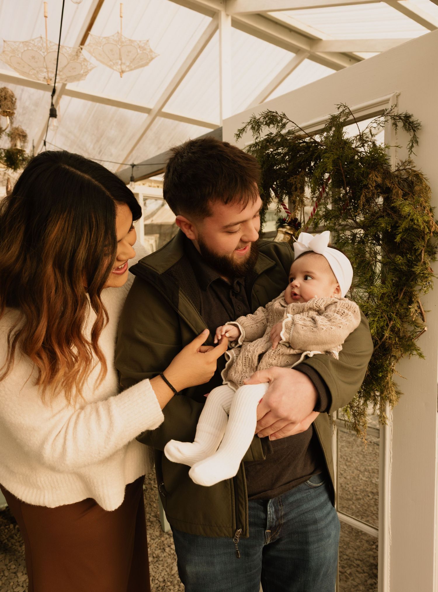 Happy young couple admiring their baby girl in decorated greenhouse setting.