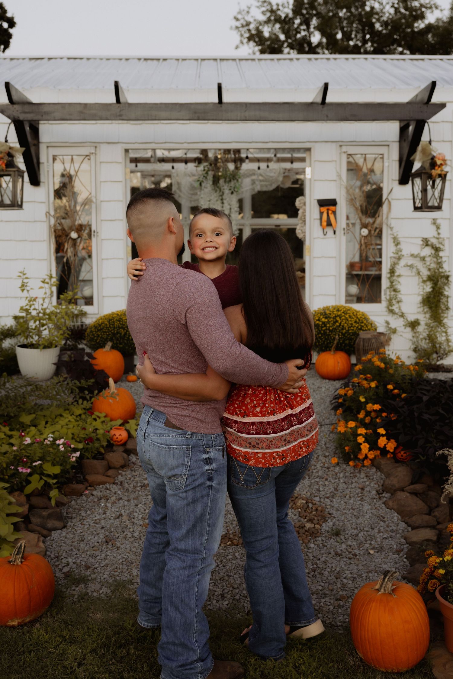 A loving family of three shares a warm embrace outdoors surrounded by fall pumpkin decorations.