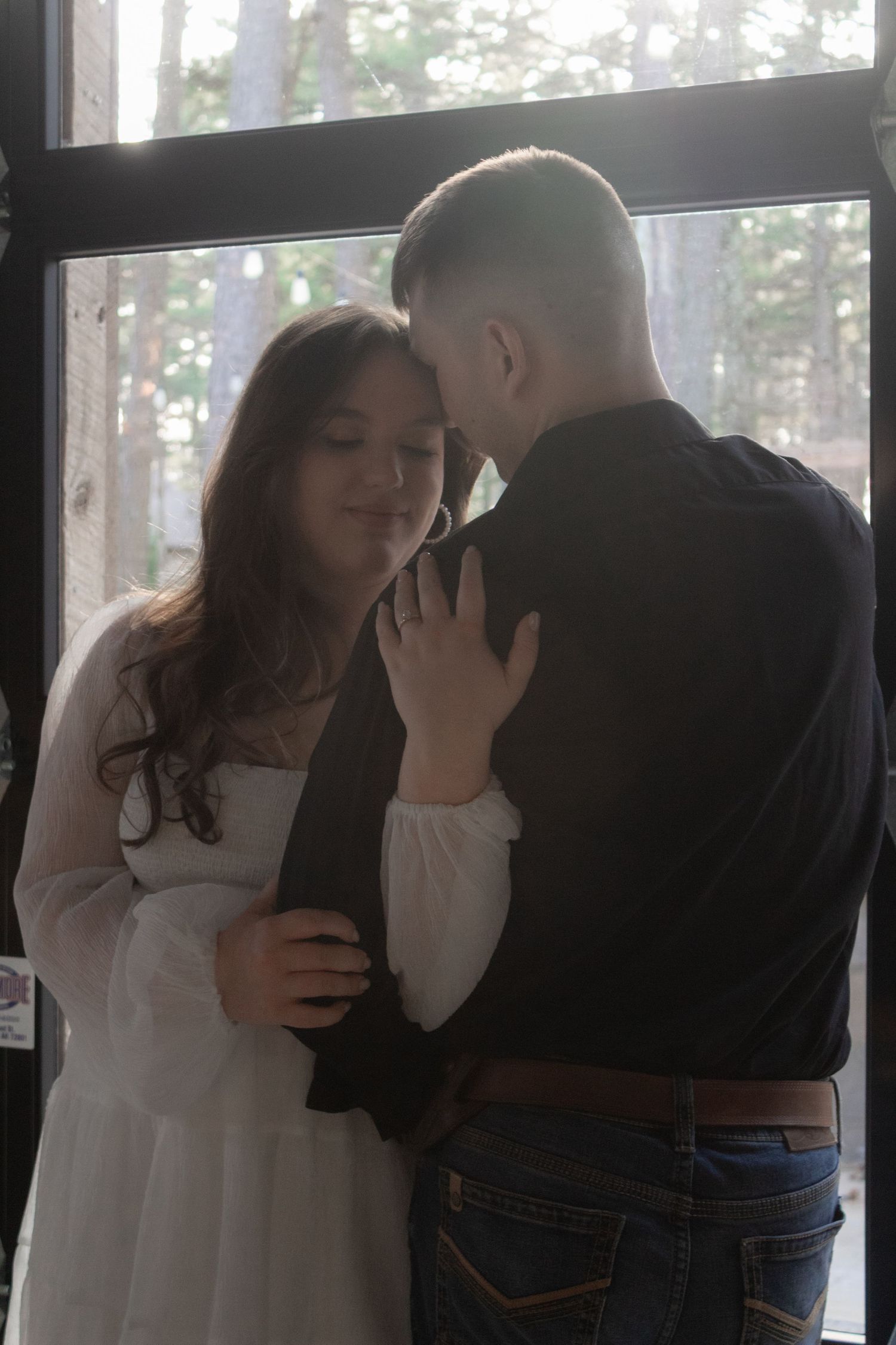 Romantic couple sharing an intimate moment by a sunlit window surrounded by trees.