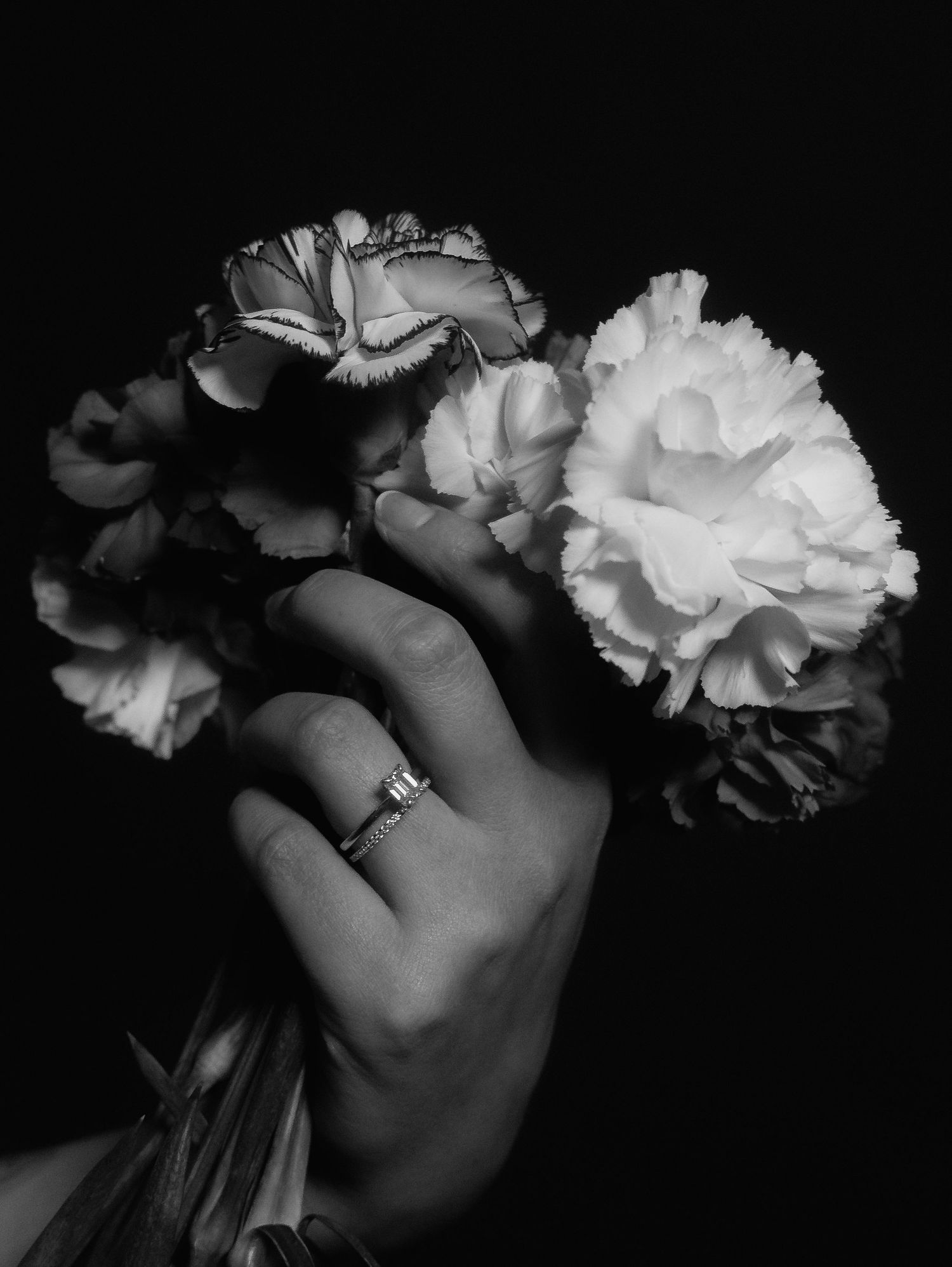 Black and white photo of hand holding carnation bouquet with diamond engagement ring.
