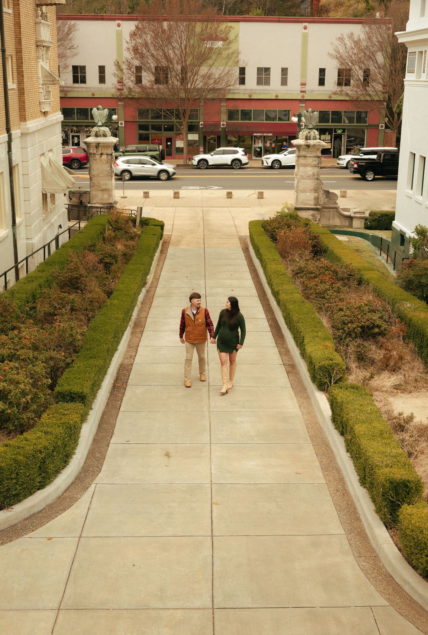 A couple walks hand in hand down a tree-lined pathway toward a charming downtown street.