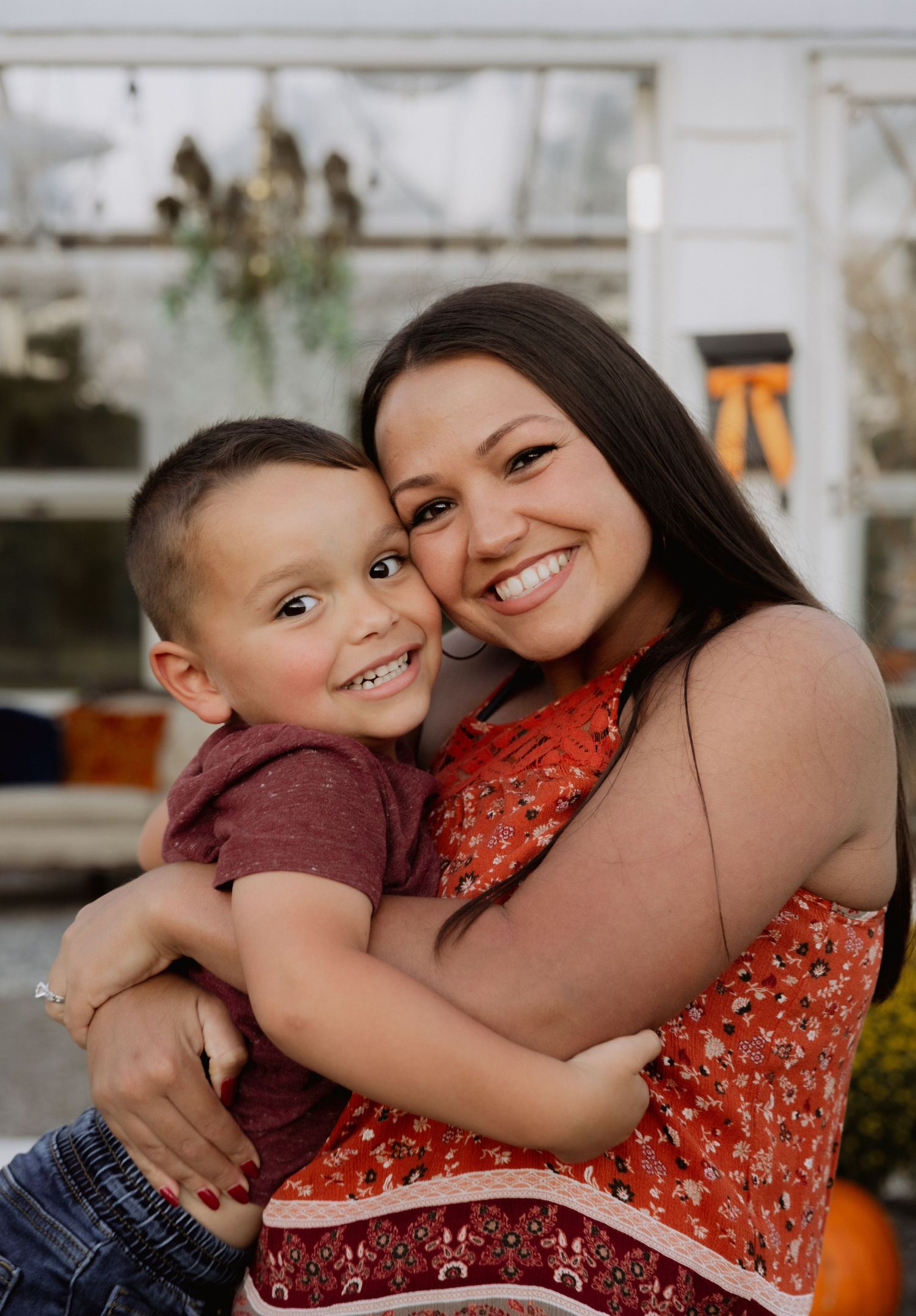 A smiling mother lovingly holds her young son outdoors near autumn pumpkin decorations.