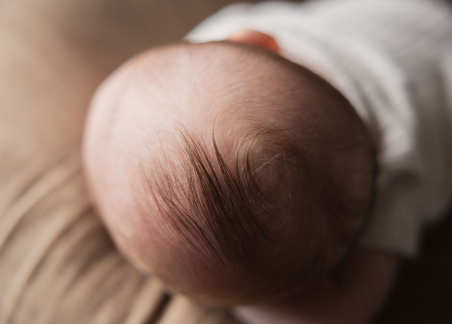 Close-up of a newborn baby's head with fine dark hair swirls against soft skin.
