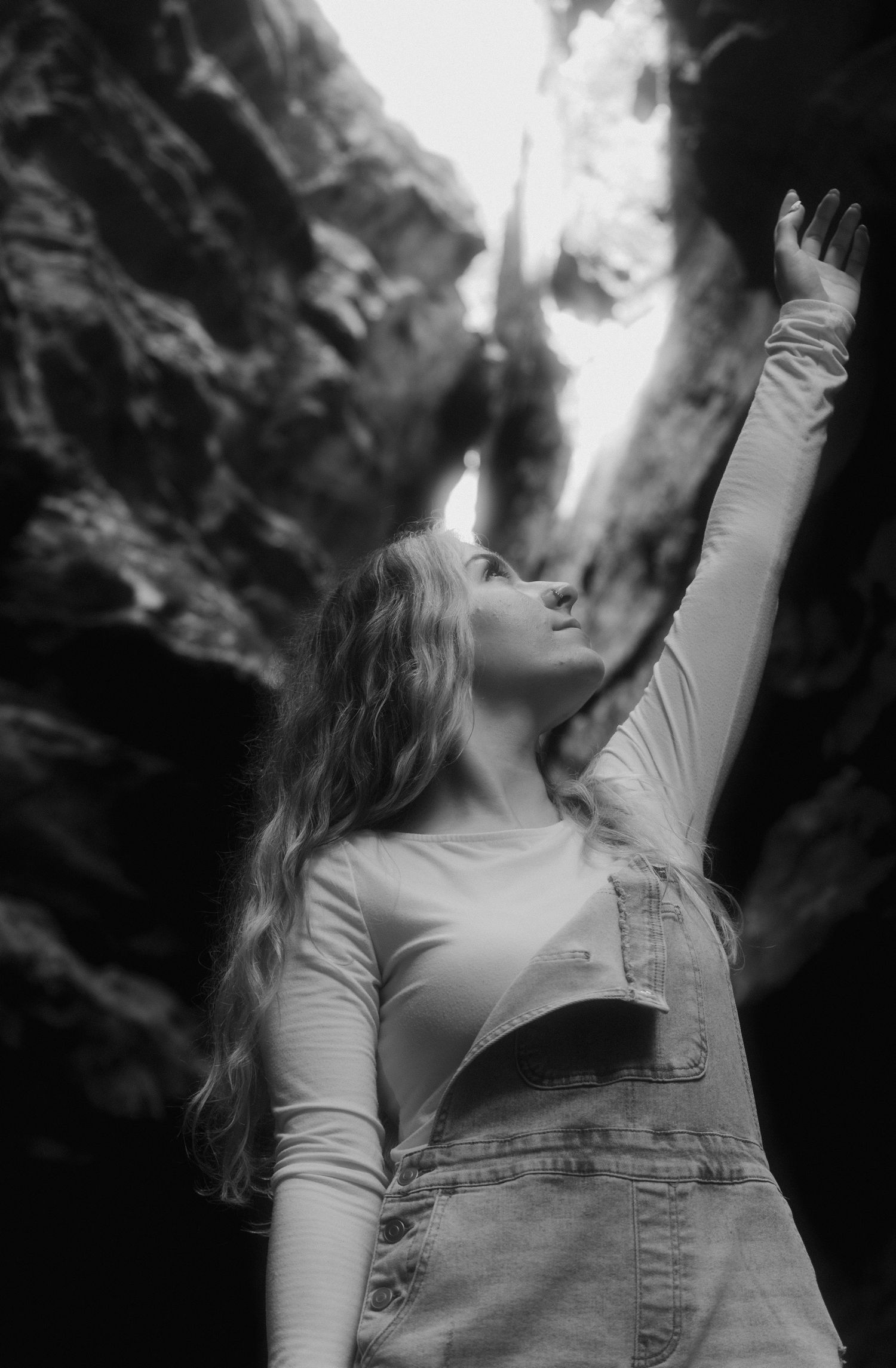 Black and white photo of woman in overalls reaching upward between dramatic rock formations.