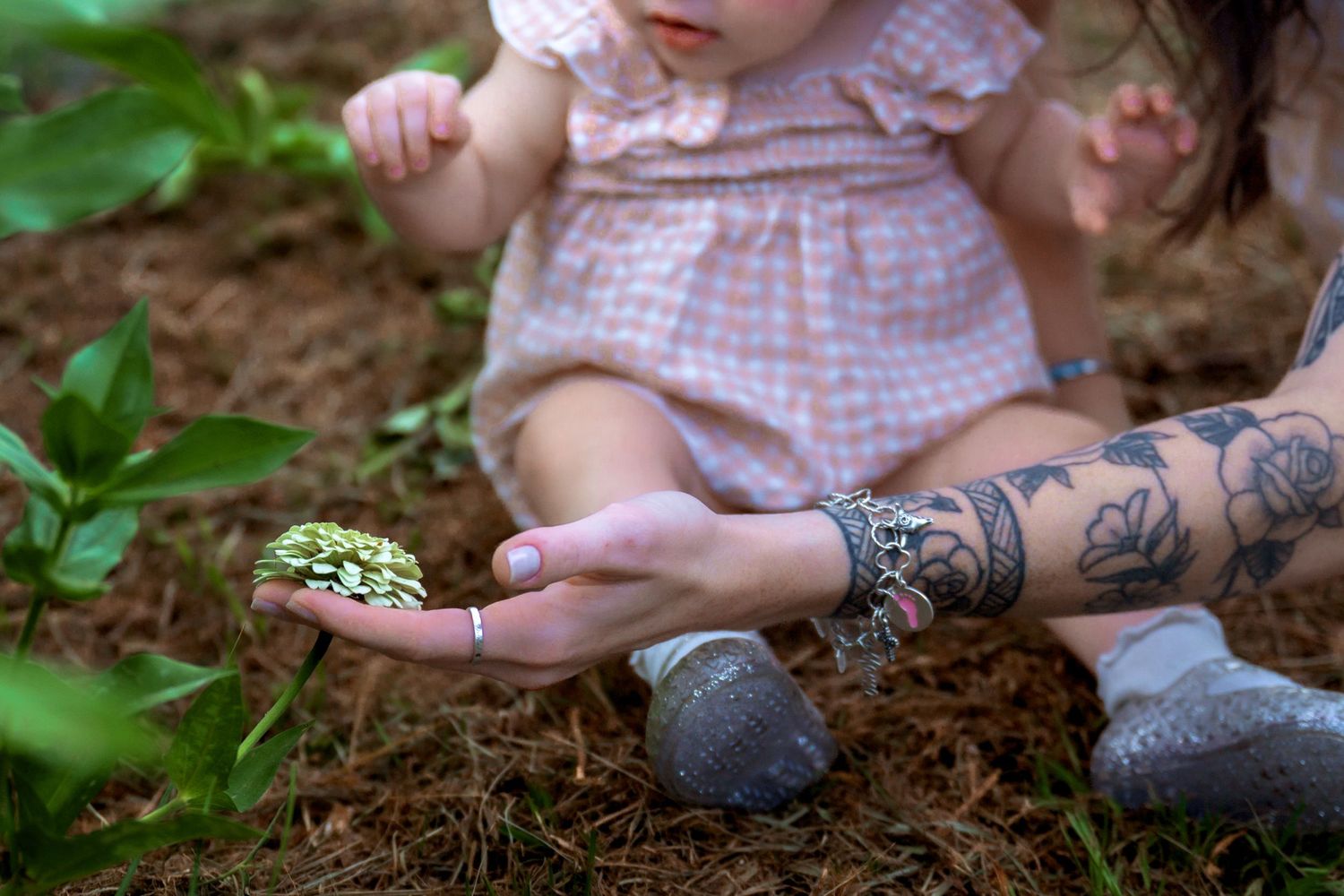 Tattooed mother shows baby a turtle in a garden setting.