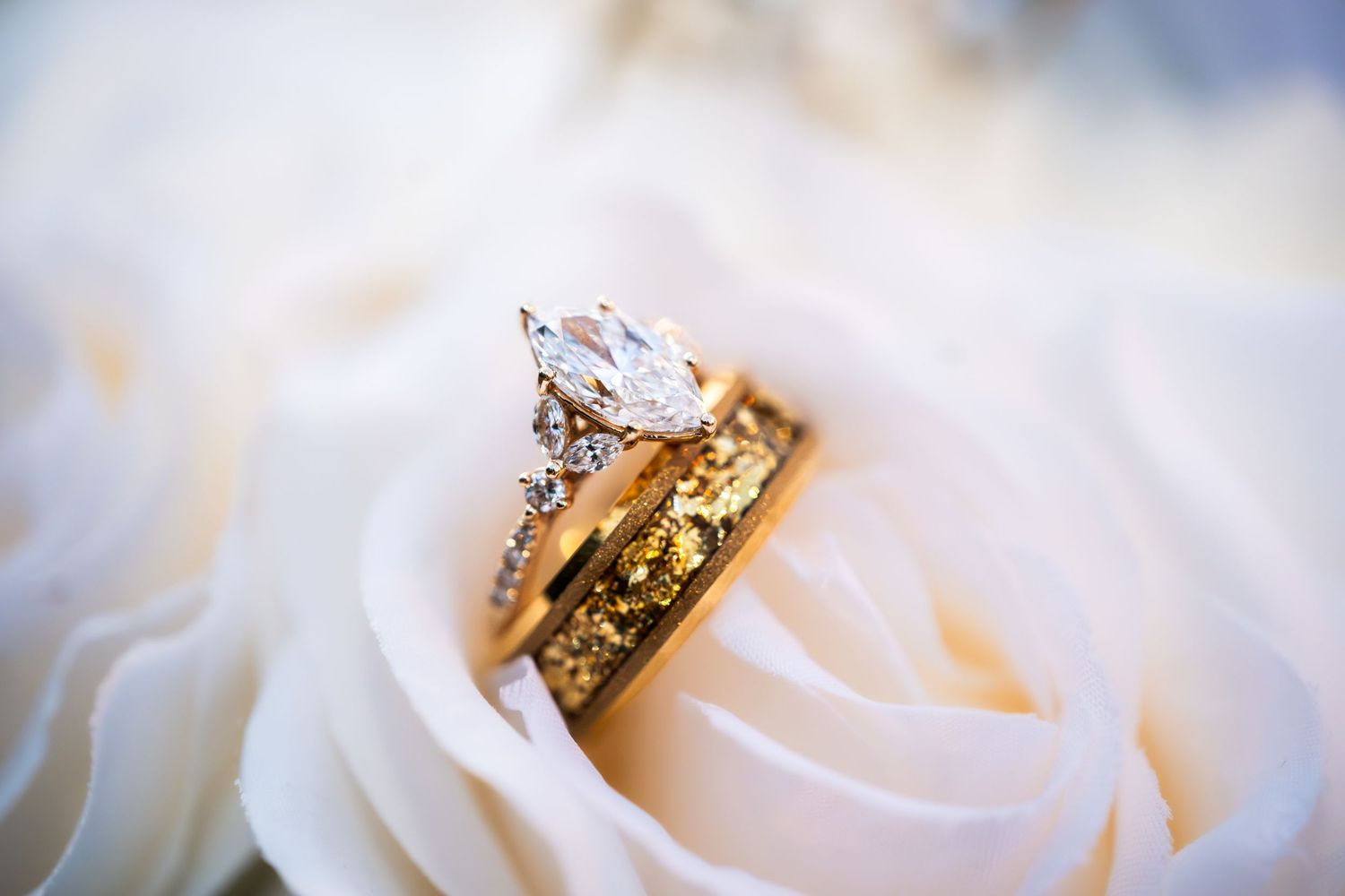 Gold marquise diamond engagement ring with wedding band on white roses.