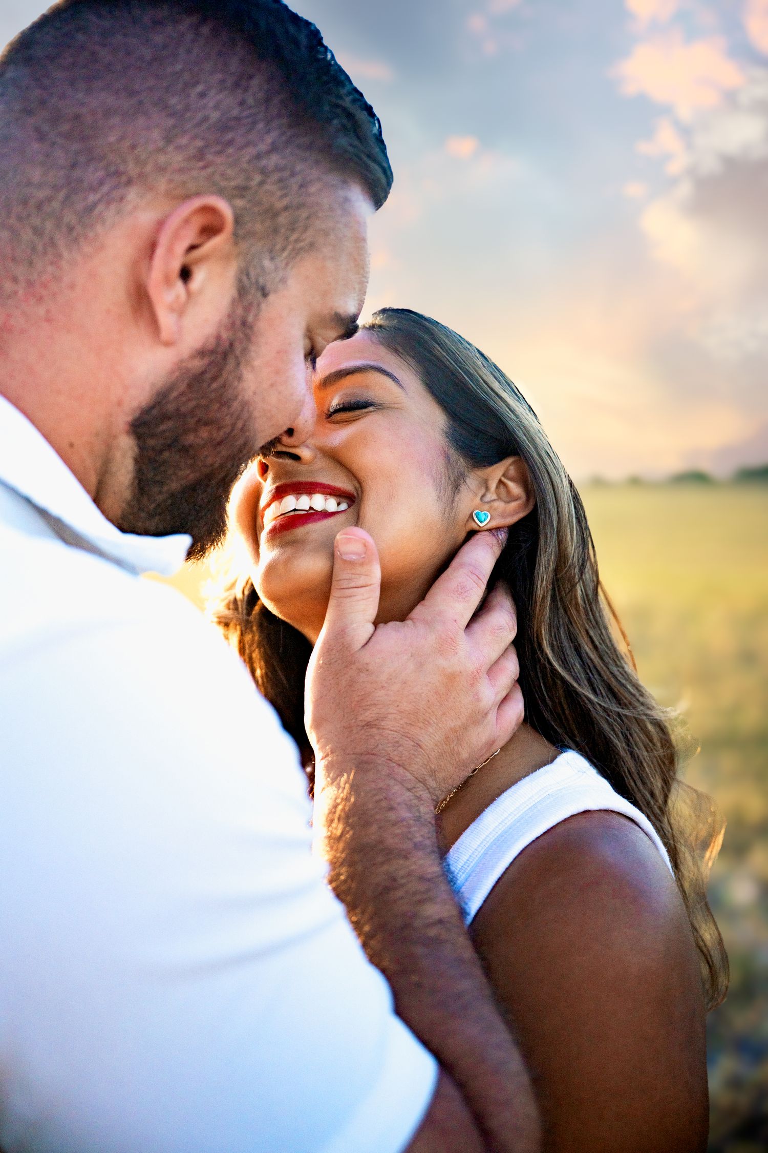 Couple sharing a romantic moment outdoors at sunset, man tenderly holding womans face as she smiles joyfully.