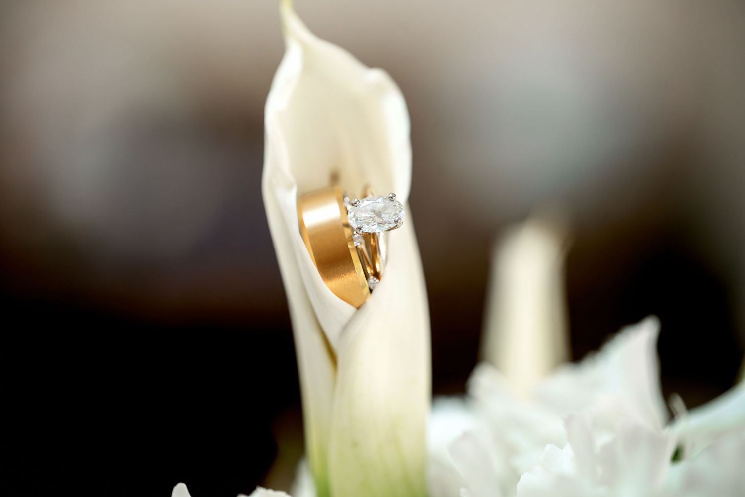 Gold wedding band and diamond engagement ring nestled in a white calla lily bloom.