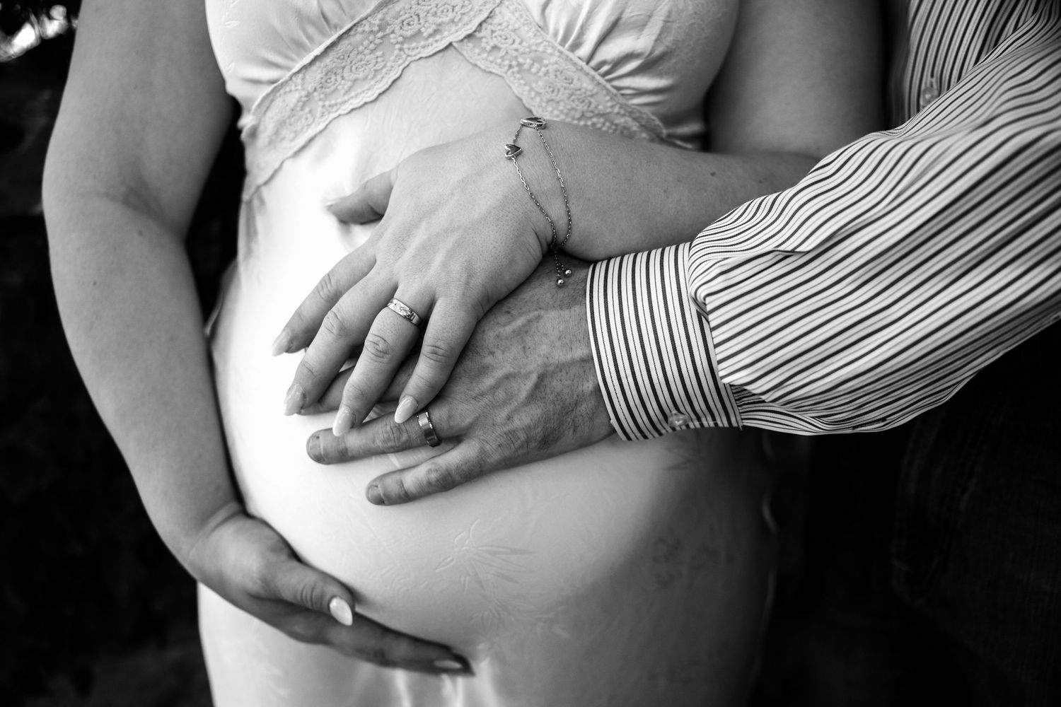 Black and white photo of a pregnant woman with her partner's hands gently cradling her baby bump.