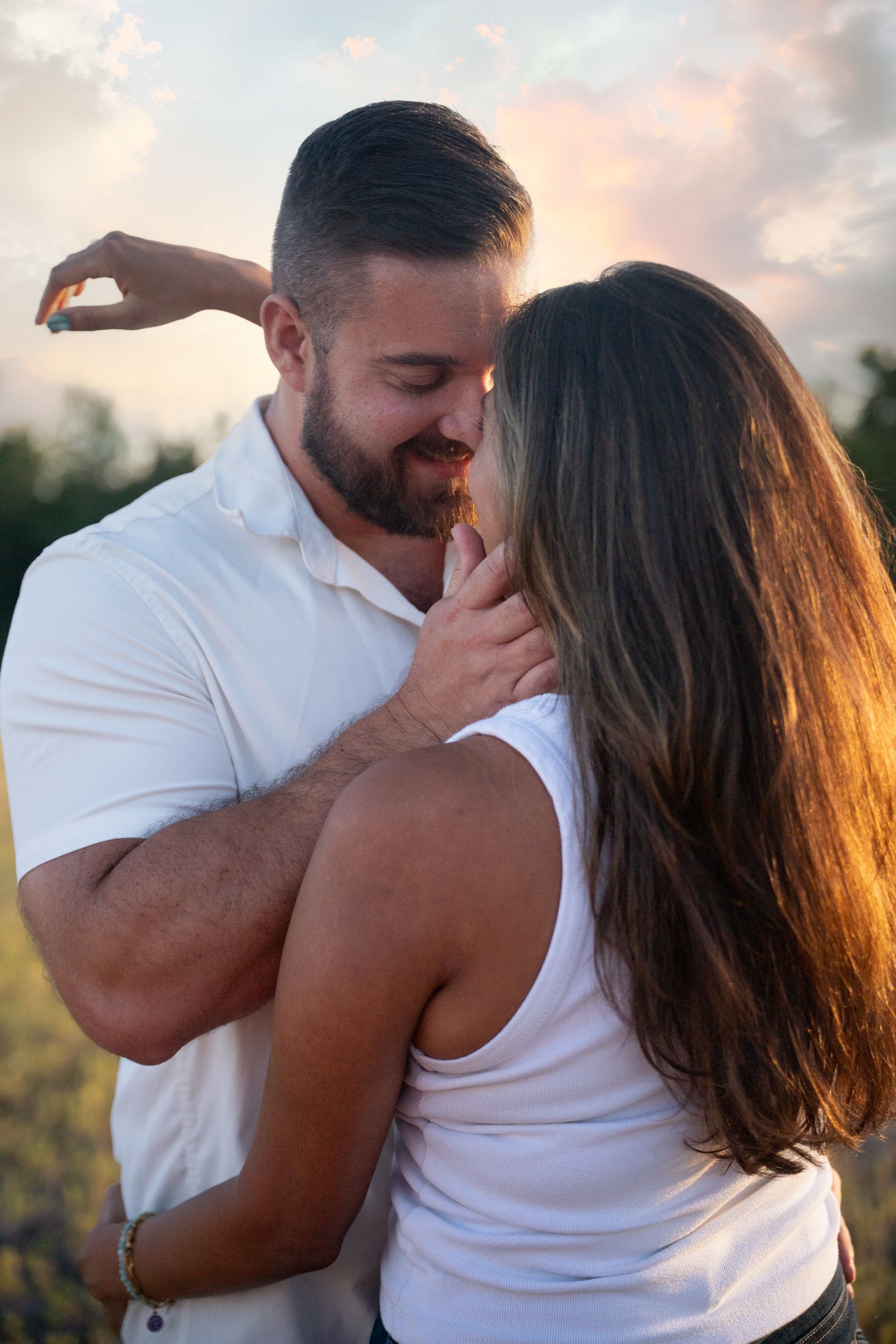 Couple in white shirts sharing a romantic moment outdoors at golden hour sunset.